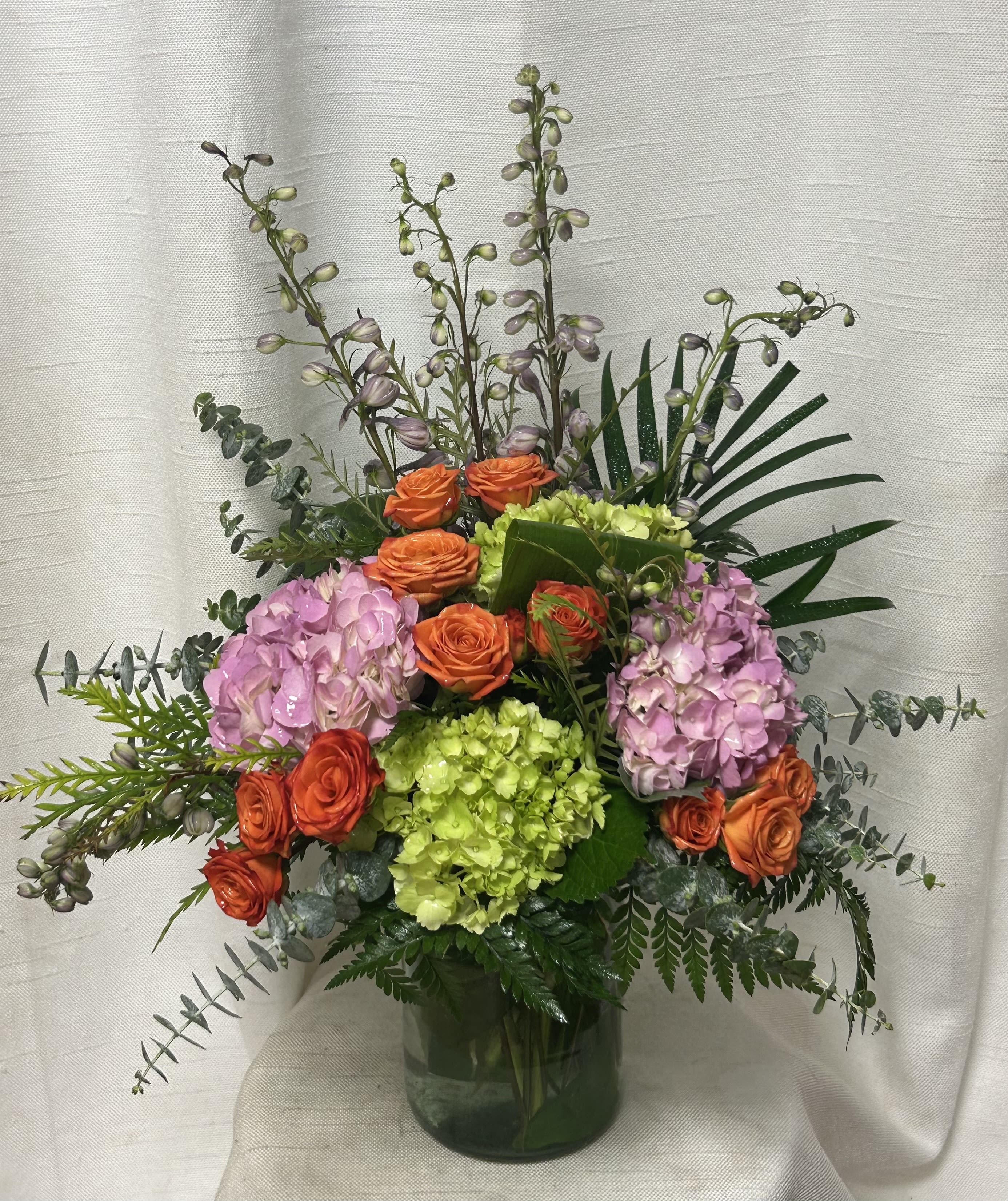 Marvelous Delight (BB) - An Enchanting Floral Arrangement with Blue Delphinium, Blue Hydrangea, Red Hypericum, Orange Roses, and Orange Tulips  This enchanting floral arrangement captivates with a harmonious blend of vibrant blue delphinium and hydrangea, complemented by the fiery hues of red hypericum, orange roses, and orange tulips. Each flower in this composition is carefully selected to evoke a sense of beauty, passion, and balance, creating a stunning display that honors the uniqueness and spirit of the departed.