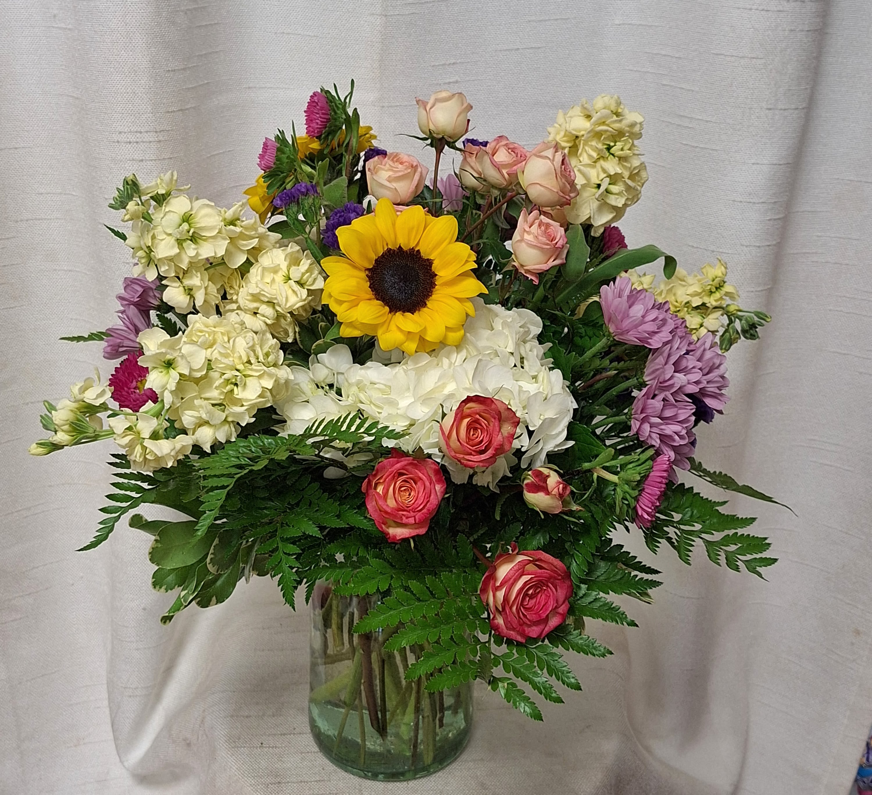 Colorful Surprise Colorful Surprise - A Stunning Floral Arrangement in Shades of Moon, Green, Yellow, Hot Pink, and Orange This captivating flower arrangement exudes a harmonious blend of elegance, vibrance, and sheer beauty. It features a delightful combination of carefully selected blooms, including three stems of moon carnations, lush green hydrangea, green lisianthus, cheerful yellow daisy poms, dazzling hot pink roses, and radiant orange roses. Together, these blooms create an extraordinary symphony of colors, textures, and fragrances that will enchant and captivate all who behold them.