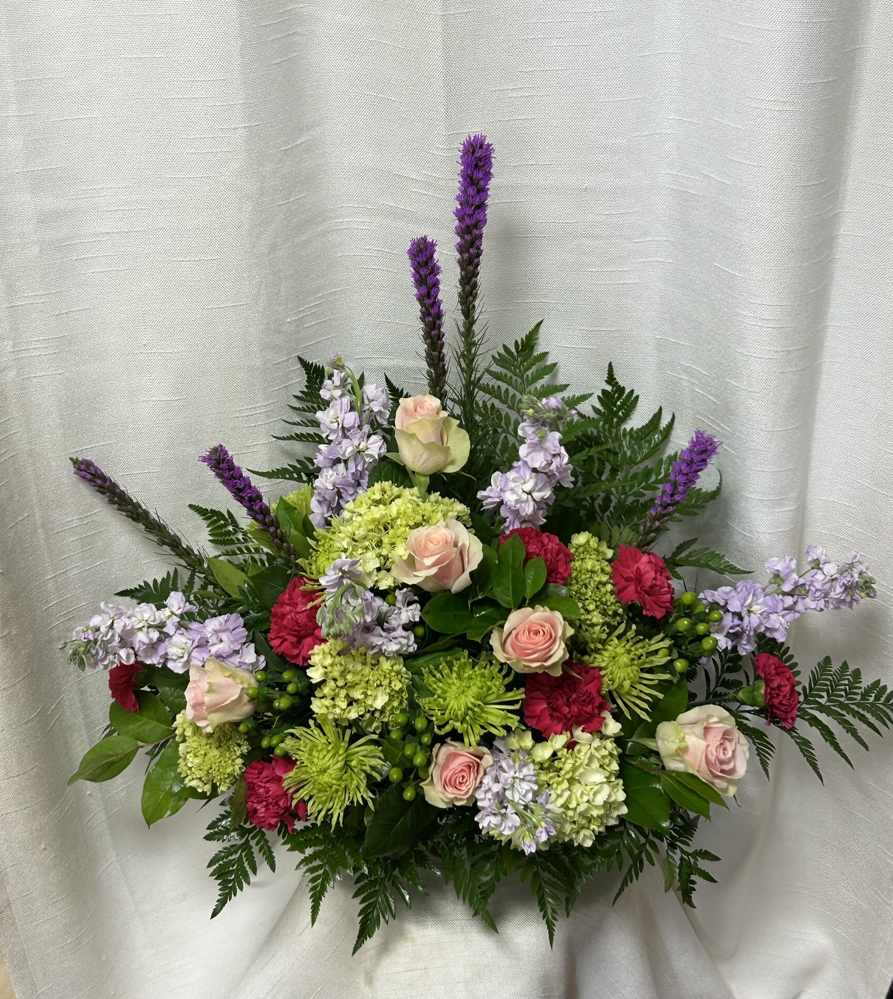Warm Caress (BB) - Create a heartfelt tribute with our funeral flower arrangement, featuring a delicate combination of green Fuji mums, purple stock, hot pink roses, hot pink carnations, hot pink mini carnations, green hypericum berries, and lush greenery. This stunning arrangement conveys a message of love, remembrance, and sympathy, honoring the life and memory of your loved one.