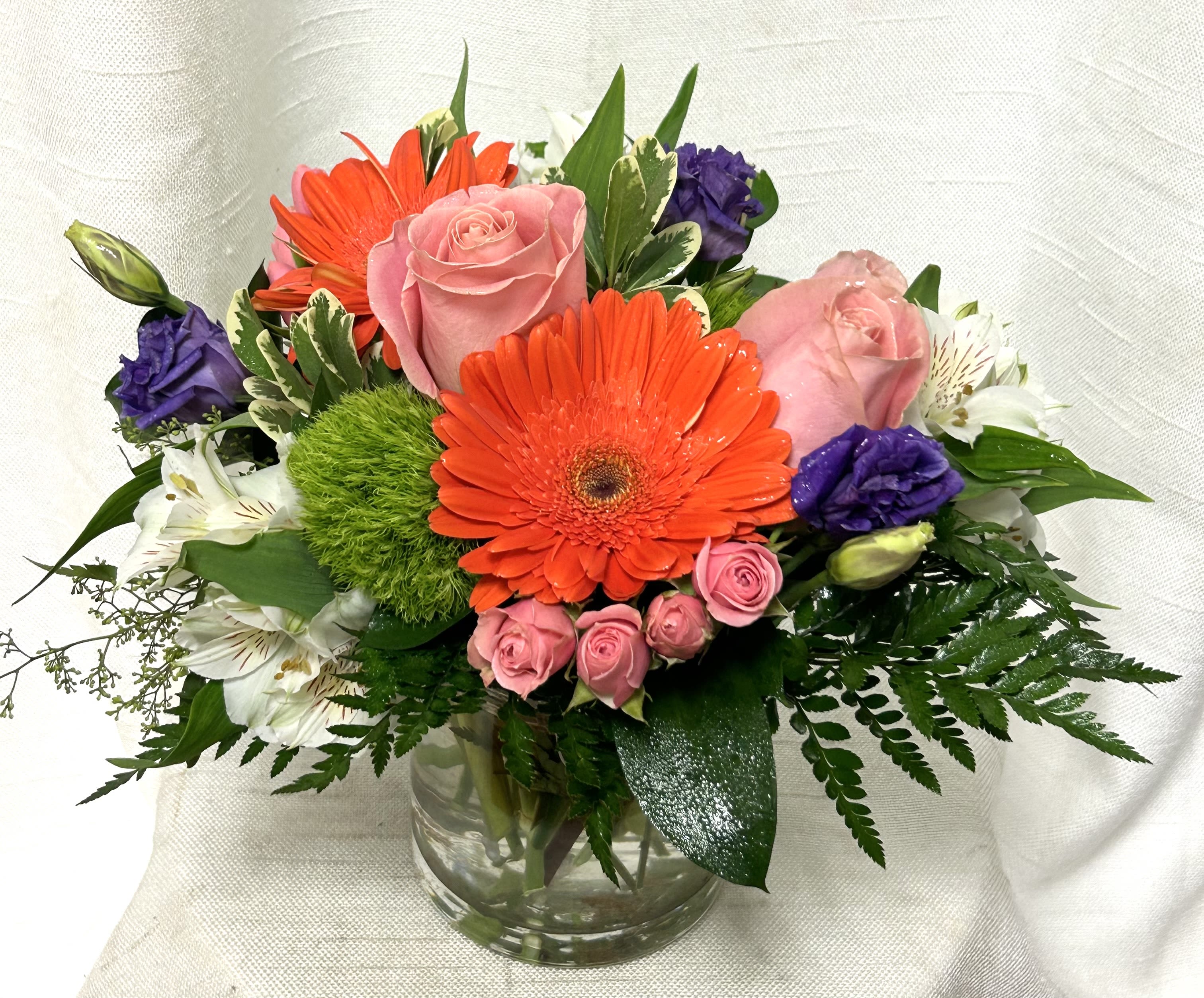 Warm Welcome (BB) Warm Welcome (BB) - Experience the heartwarming embrace of "Feels Like Home," a captivating arrangement that effortlessly brings comfort, warmth, and a sense of belonging. This beautiful bouquet showcases a stunning combination of pink roses, orange gerbera daisies, and green balls, artistically arranged in a clear glass vase.