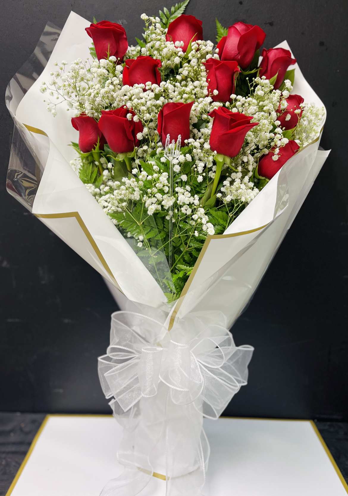 BF-E335 Presentation Bouquet 1 Dz. Red Roses  - Introducing our One Dozen Red Roses Presentation Bouquet, adorned with a Red Bow, Baby's Breath, and Lemon Leaf, lovingly encased in a Cellophane Wrap – A Timeless Expression of Love and Elegance: