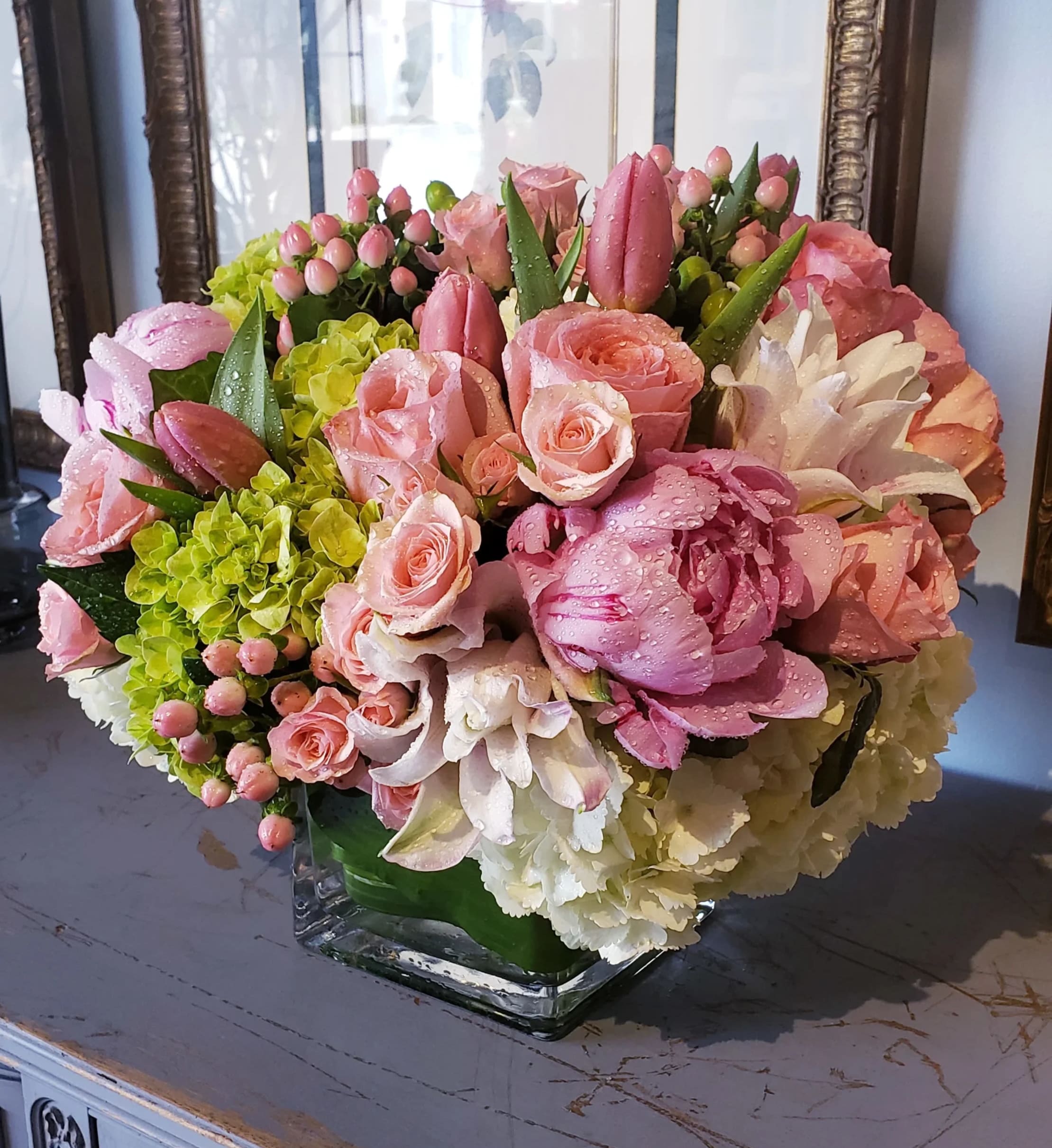 Spring in Paris - Transport yourself to a Parisian garden in springtime with this luxurious and romantic arrangement. Nestled in a modern clear glass cube, Spring in Paris features a lush blend of soft white and green hydrangeas, fragrant pink garden roses, delicate peonies, elegant lilies, and blush spray roses. Accents of pink hypericum berries and artistically wrapped aspidistra leaves complete this fresh, feminine design—perfect for celebrating love, beauty, and new beginnings.  Please note: Flower varieties and container style may vary based on seasonal availability, while always maintaining the overall aesthetic and value.  Freshness Guarantee: At Belden's Florist, we stand behind the quality of every arrangement. Our flowers are guaranteed to remain fresh and beautiful for 3–5 days after delivery. To extend their life, we recommend adding clean water daily. Just like us, flowers thrive with hydration—keeping them nourished helps them bloom beautifully for as long as possible.
