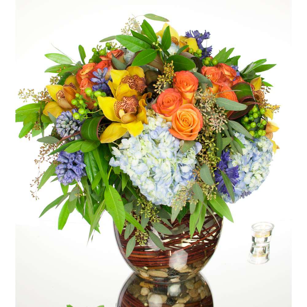 Tranquil Sunsets (DB) Tranquil Sunsets (DB) - Elevate your space with our upscale modern flower arrangement, thoughtfully designed with a lively mix of floral textures and a stunning color palette. This captivating arrangement showcases beautiful blue hydrangeas, vibrant orange roses, sunny yellow cymbidium orchids, charming green hypericum, fragrant hyacinth, and whimsical seeded eucalyptus.
