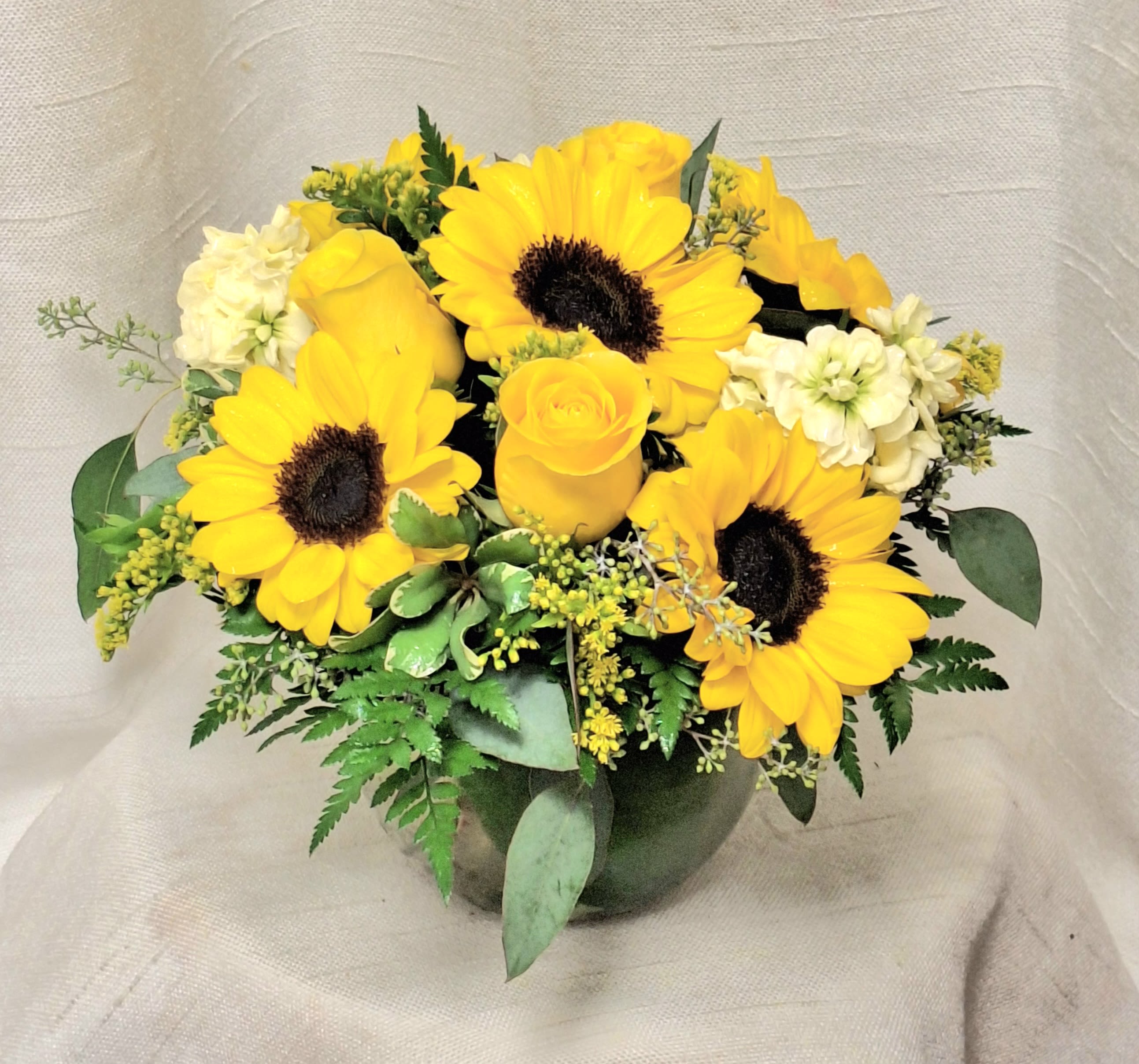 Sunshine Meadows (DB) Sunshine Meadows (DB) - Step into a radiant oasis of warmth and cheer with our "Sunshine Meadows" arrangement. This captivating ensemble showcases the golden splendor of sunflowers, yellow roses, yellow stock, and yellow solidago, reminiscent of a picturesque meadow bathed in sunlight.