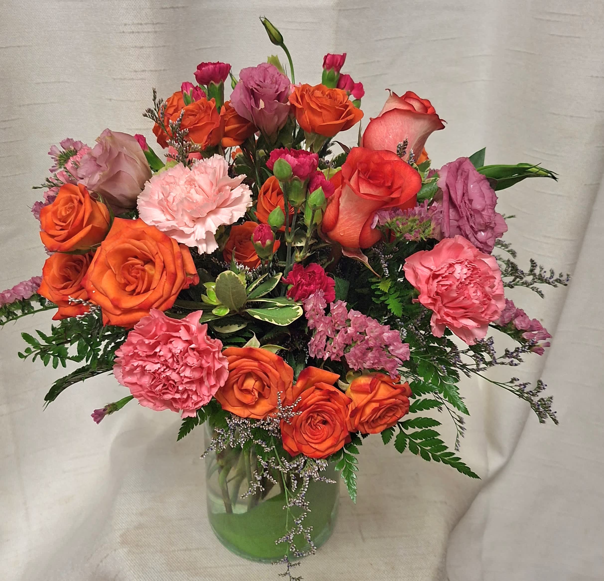 Dreaming - .Indulge in the vibrant hues of our Orange, Pink, and Hot Pink Flower Arrangement, a stunning ensemble of orange roses, pink lisianthus, orange spray roses, pink statice, and pink carnations. Expertly arranged in a clear glass vase, this captivating medley exudes a perfect blend of warmth and elegance. Elevate any space with this colorful bouquet that promises to brighten every moment. 