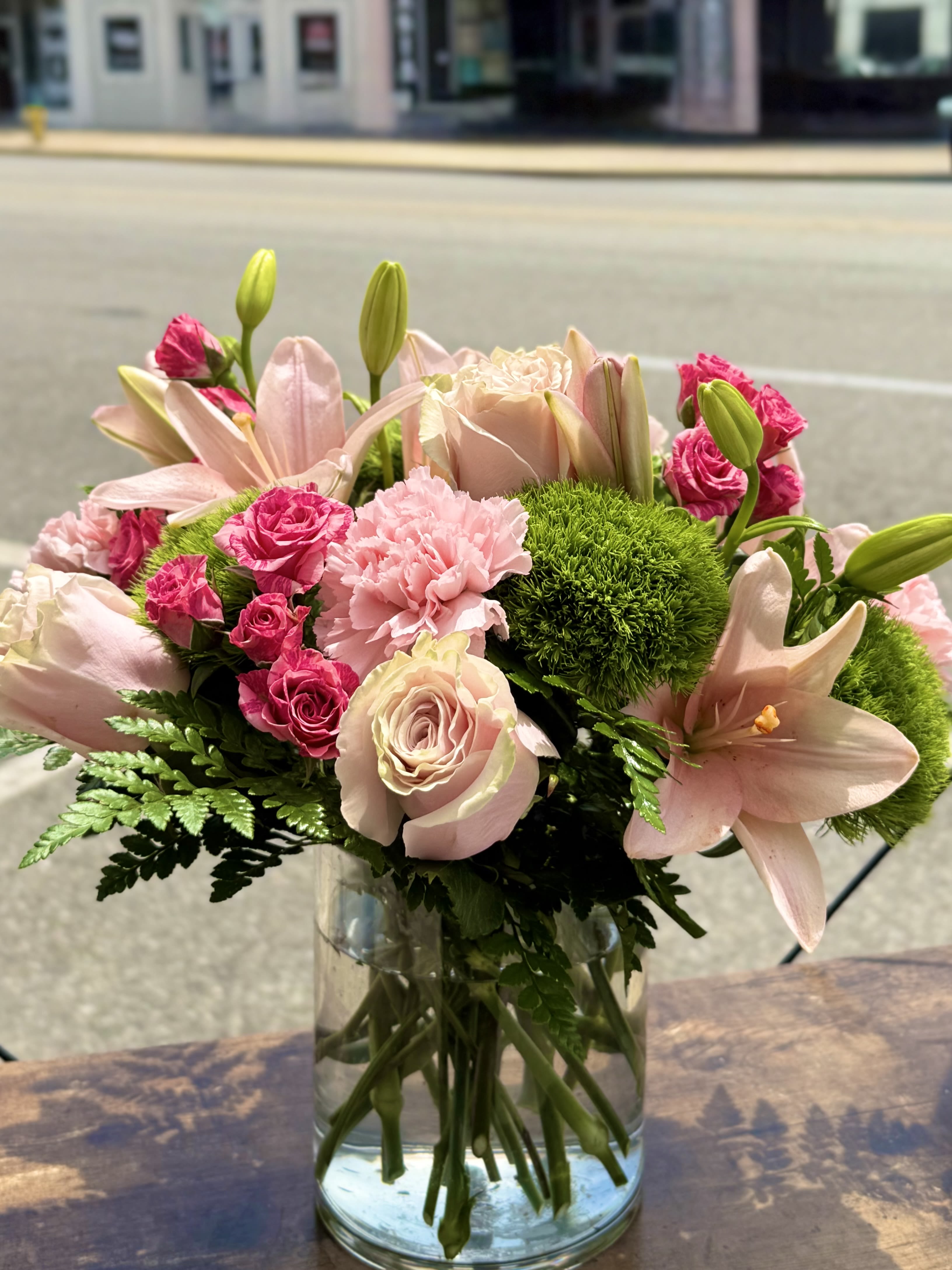 Stella Monroe Stella Monroe - Pretty pinks, roses, lily's spray roses, carnations and greens designed in a glass cylinder.