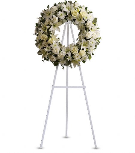 Serenity Wreath Standing Spray - A ring of bright and fragrant white blossoms create a serene expression of sympathy. Laid on a beautiful bed of assorted greenery, elegant white roses, lilies, and carnations come together to create a thoughtful and compassionate display.