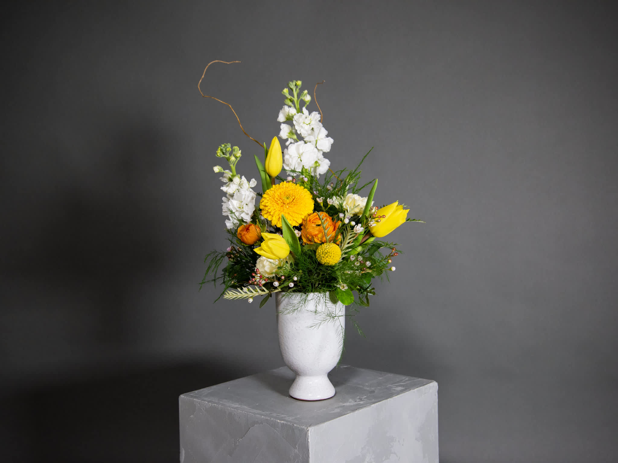 Okanagan Valley, Wanderlust Series - Ceramic Pot Arrangement Okanagan Valley, Wanderlust Series - Ceramic Pot Arrangement - The Okanagan Valley arrangement is one of our most popular arrangements from our Wanderlust series. It embodies the warmth and colours of spring in one of the most beautiful regions of Canada. This floral arrangement that is full of sunny vibes makes the perfect gift to brighten someones day. It is comprised of fragrant white stock, yellow tulips, orange ranunculus, scabiosas, white carns, craspedia, curly willow, micro wax flowers and an assortment of green foliage. Pot size : 4in X 6.25in