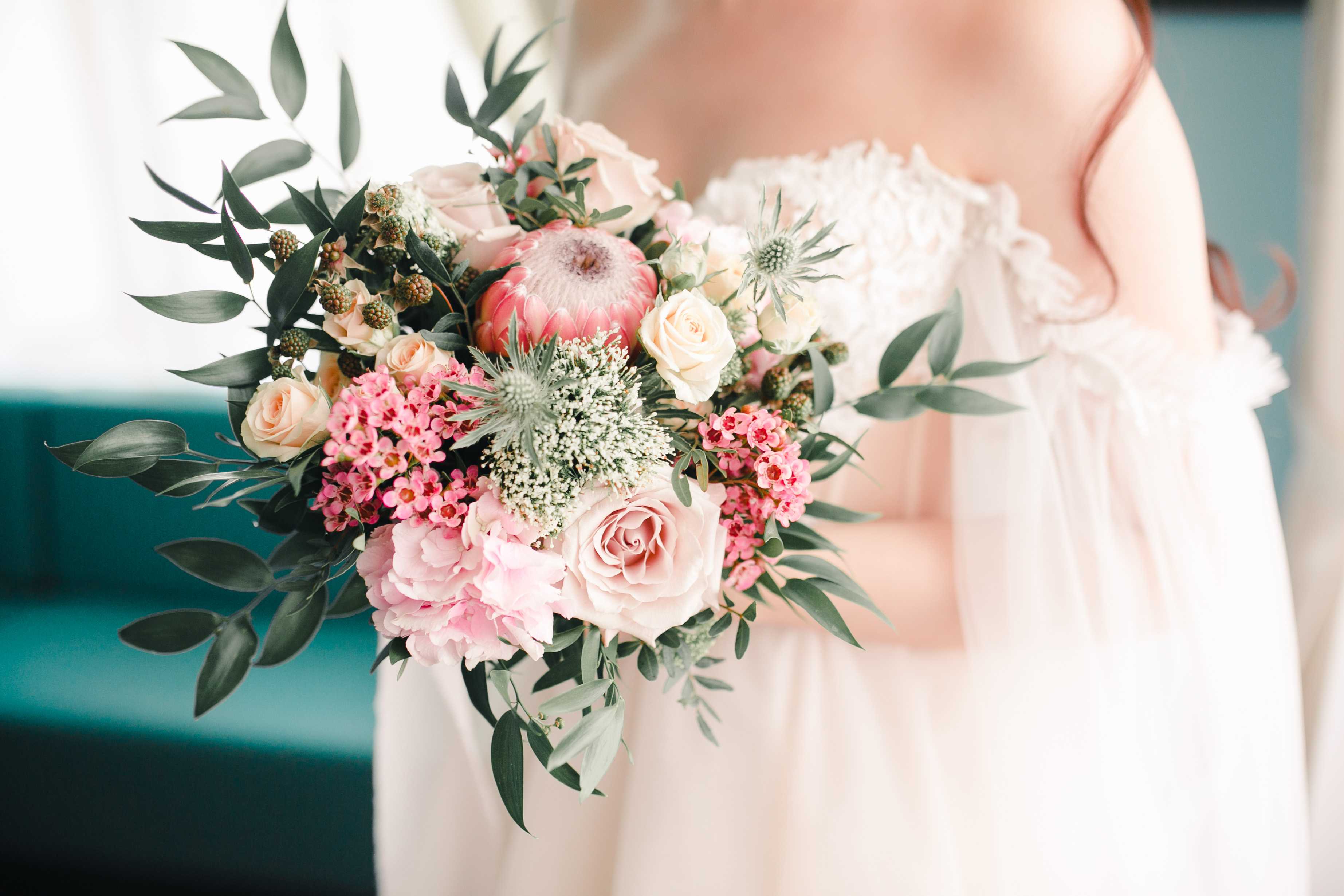 Freyja – Bridal Bouquet (Price varies by custom design) - The Freyja bridal bouquet is a refined and romantic arrangement designed to complement the modern bride. Featuring soft blush roses, delicate pink hydrangeas, and charming clusters of wax flowers, it’s beautifully accented with lush greenery and a striking protea centerpiece—bringing together timeless elegance and natural beauty.  The price listed is an average estimate, as final pricing may vary depending on bouquet size, flower selection, and seasonal availability.  To receive a personalized quote and start designing your dream wedding florals, please contact our store directly. We’d love to create something uniquely beautiful just for you.