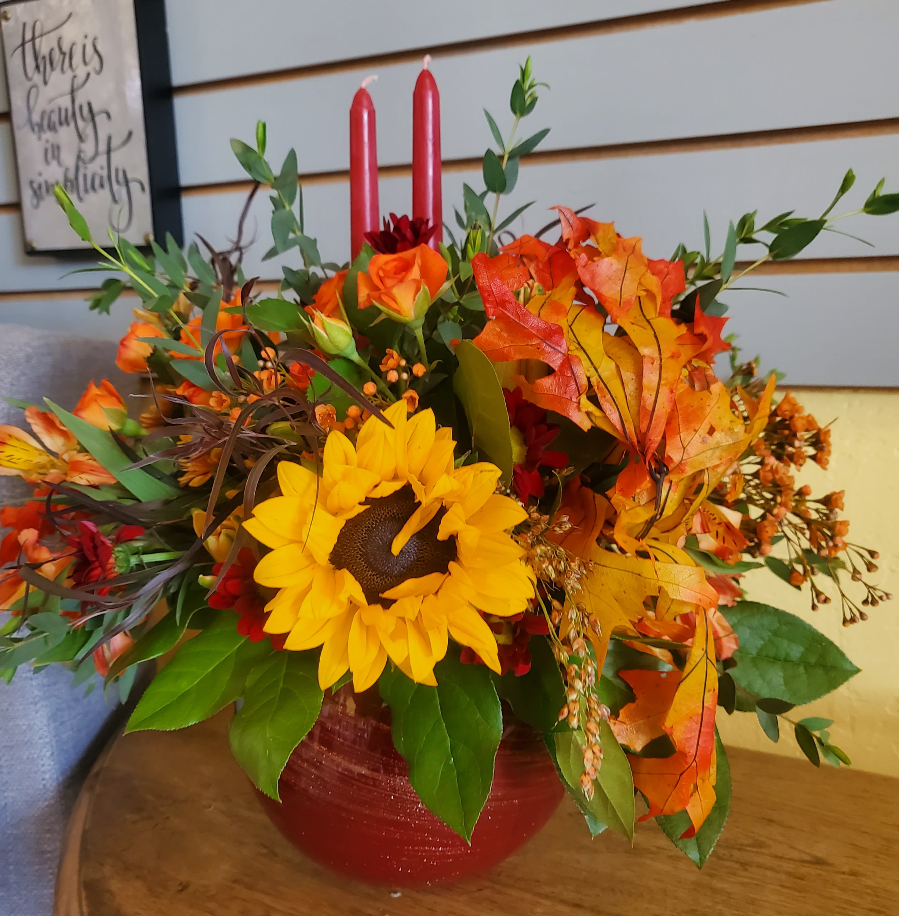 Grateful Grateful - This festive centerpiece is designed in a red container using our most fall themed florals such as sunflowers, red roses, orange alstro, and bronze buttons.