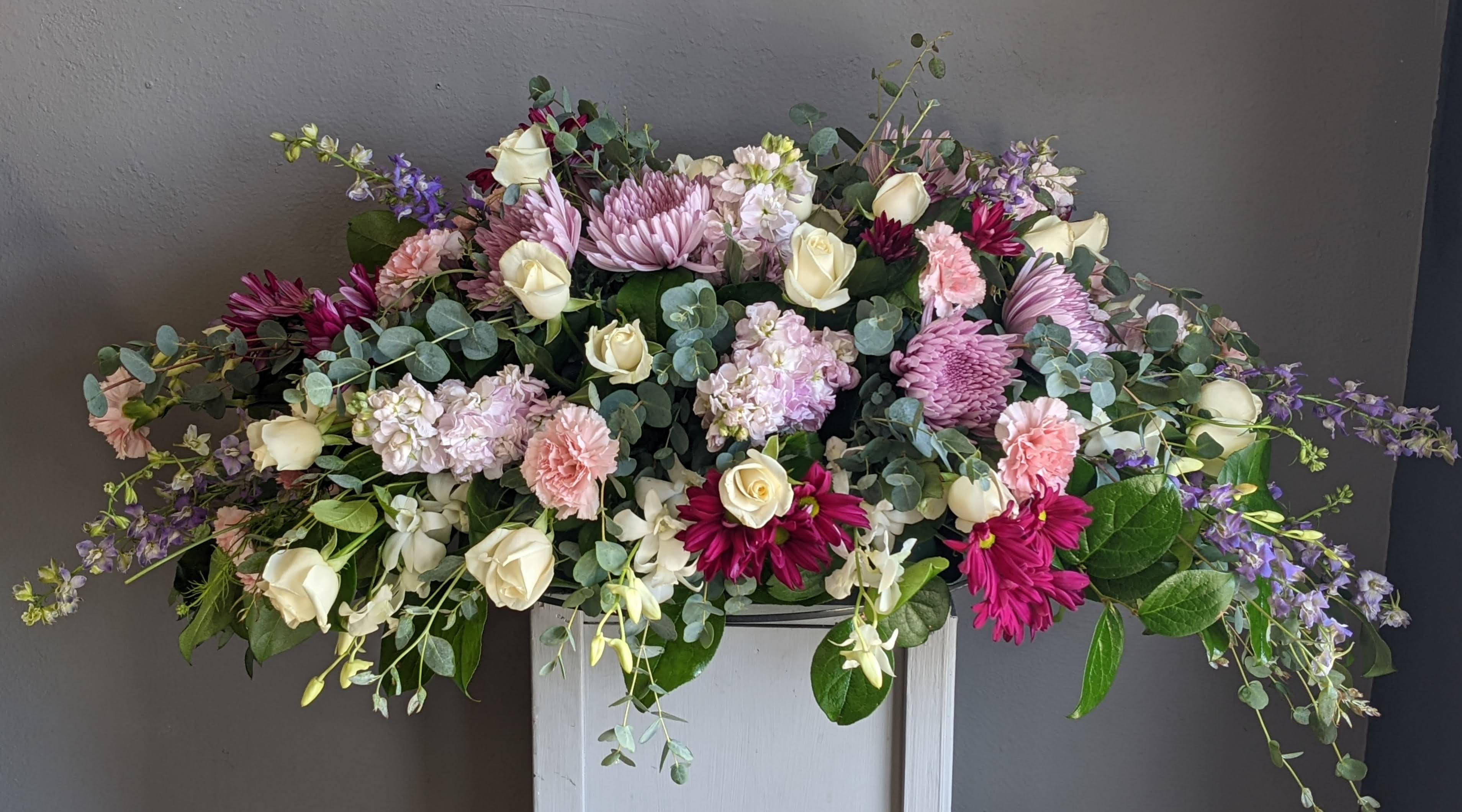 FUNERAL CASKET SPRAY - Peaceful Pastels 71 - This is a gorgeous option for a funeral service or church. This casket can be designed as a half casket or a full casket for either an open casket or a closed casket service. This soft mix of pastel roses, dendrobium orchids, stock and carnations is the perfect way to add gentle color to day of memories.   **This is a piece for a funeral or memorial service. Please place the order at least 2 days prior to the service to guarantee a certain arrangement. Anything sooner and we cannot guarantee it will match the picture. These pieces can be customized to the color of your choice. The flowers may vary depending on availability of the flowers, special requests and quality of the flowers we have in stock. If you have a special request please add it to our special instructions when placing your order. If you have any questions please don’t hesitate to call. 714 289 1123**