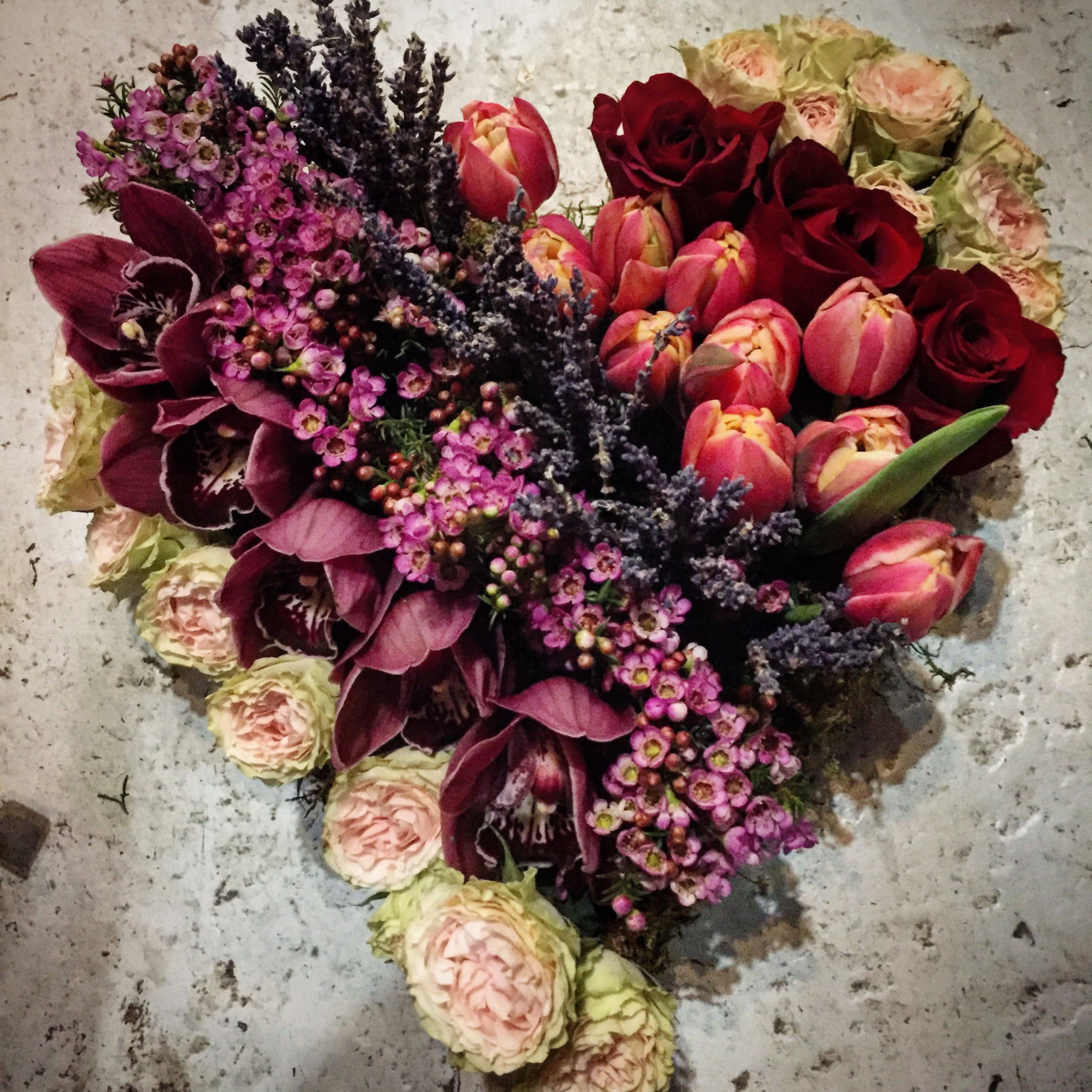 I Heart U: A stunning piece of floral artwork - ‘I Heart U’ is a Beethoven’s Veranda top seller and a most popular, unique, one of a kind piece of art design. This beautiful floral heart is filled with abundant orchids, freesia, roses, lilies and lavender as well as other premium flowers. Flowers will vary based on fresh, available blooms. This floral is simply stunning.  Please note:  The heart is hand shaped into professional floral foam which is then secured onto a foam or corrugated base. This beautiful art piece arrangement lays flat for display purposes. When watering you should water over sink. Allow to drip dry before returning to display. Always protect fine furniture with plastic before considering where to display art piece. 