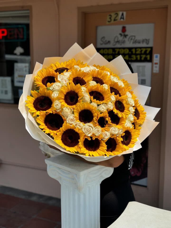 Golden Embrace - At the heart of this bouquet is a single sunflower surrounded by rings of sunflowers and white roses. A stunning blend of warmth and grace, Golden Embrace is perfect for celebrating special moments with a touch of nature's finest beauty. 