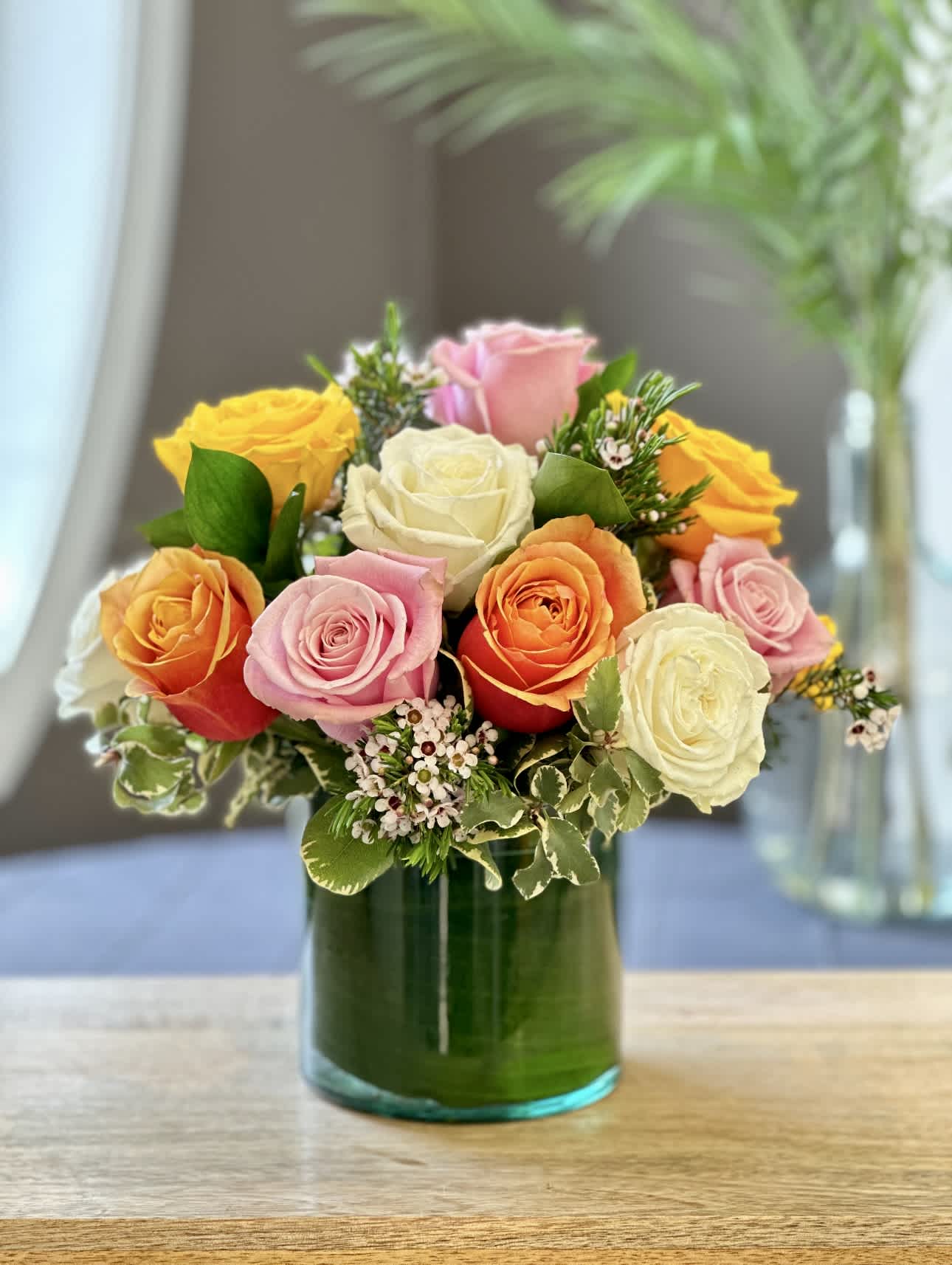 Baker's Dozen Bouquet - SPRING &amp; SUMMER COLLECTION | LOCAL DELIVERY ONLY   A colorful twist on a classic rose bouquet. This vibrant arrangement features 13 mixed-color roses with delicate accents of wax flower, designed in a leaf-wrapped clear cylinder vase. Compact and modern, it's a sweet way to show someone they're one of a kind - with a little extra love.