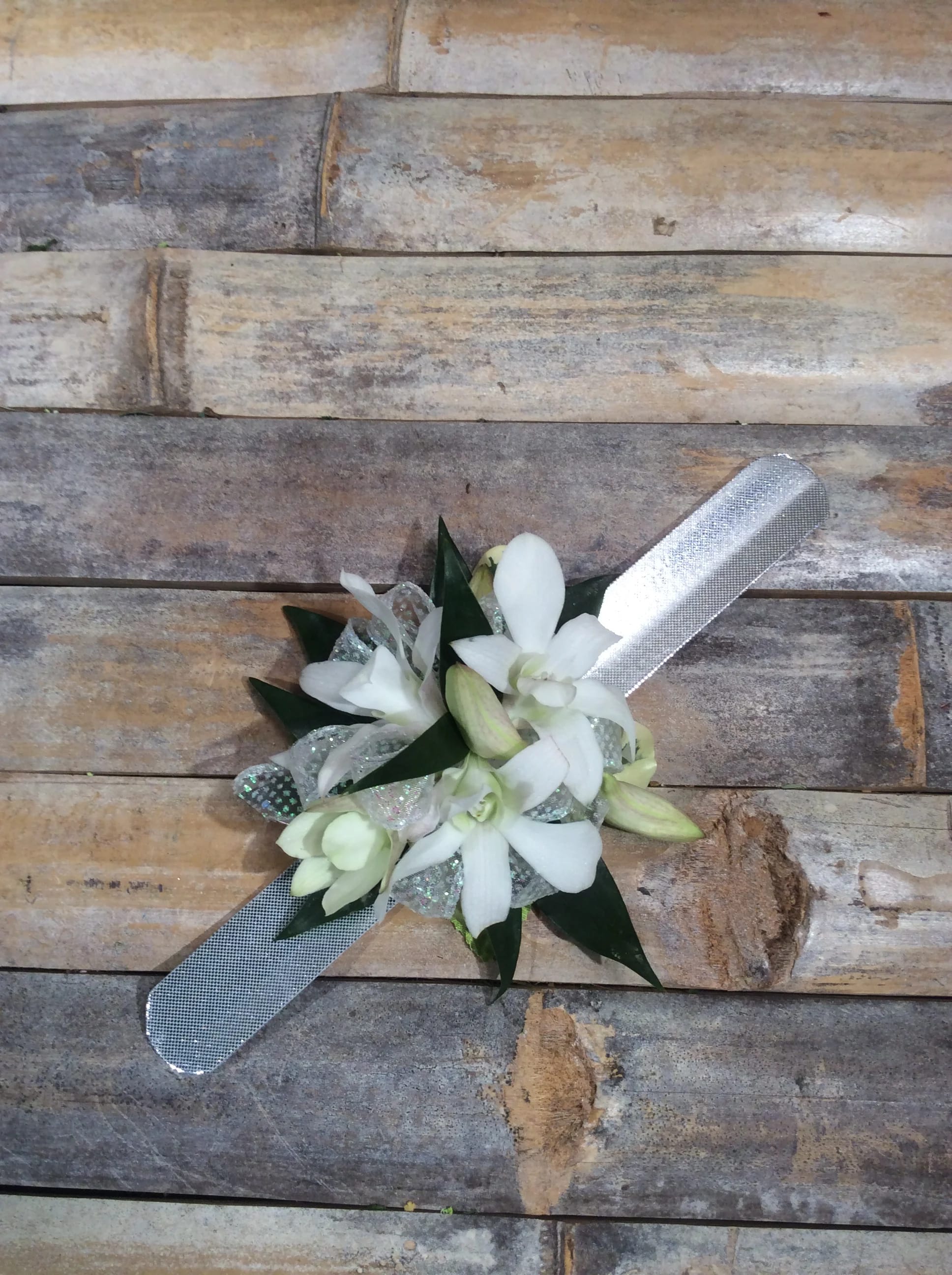 Dendrobium Orchid Corsage Dendrobium Orchid Corsage - Elevate your special day outfit with our exquisite white dendrobium orchid corsage! Each corsage is made on the slap band with delicate greenery and choice of ribbon. Color choices for the ribbons are: Sheer ribbon Accent Options: Iridescent, ,white, Cream, Soft Pink, Hot Pink, Navy Blue, Baby Blue, Royal Blue, Black, Silver, Gold, Purple, Lavender, Burgundy, Peach If you are unsure what to pick, may we suggest white rose with iridescent ribbon - goes with everything! Please let us know your color choice for the ribbon in the Florist Instruction are during checkout.