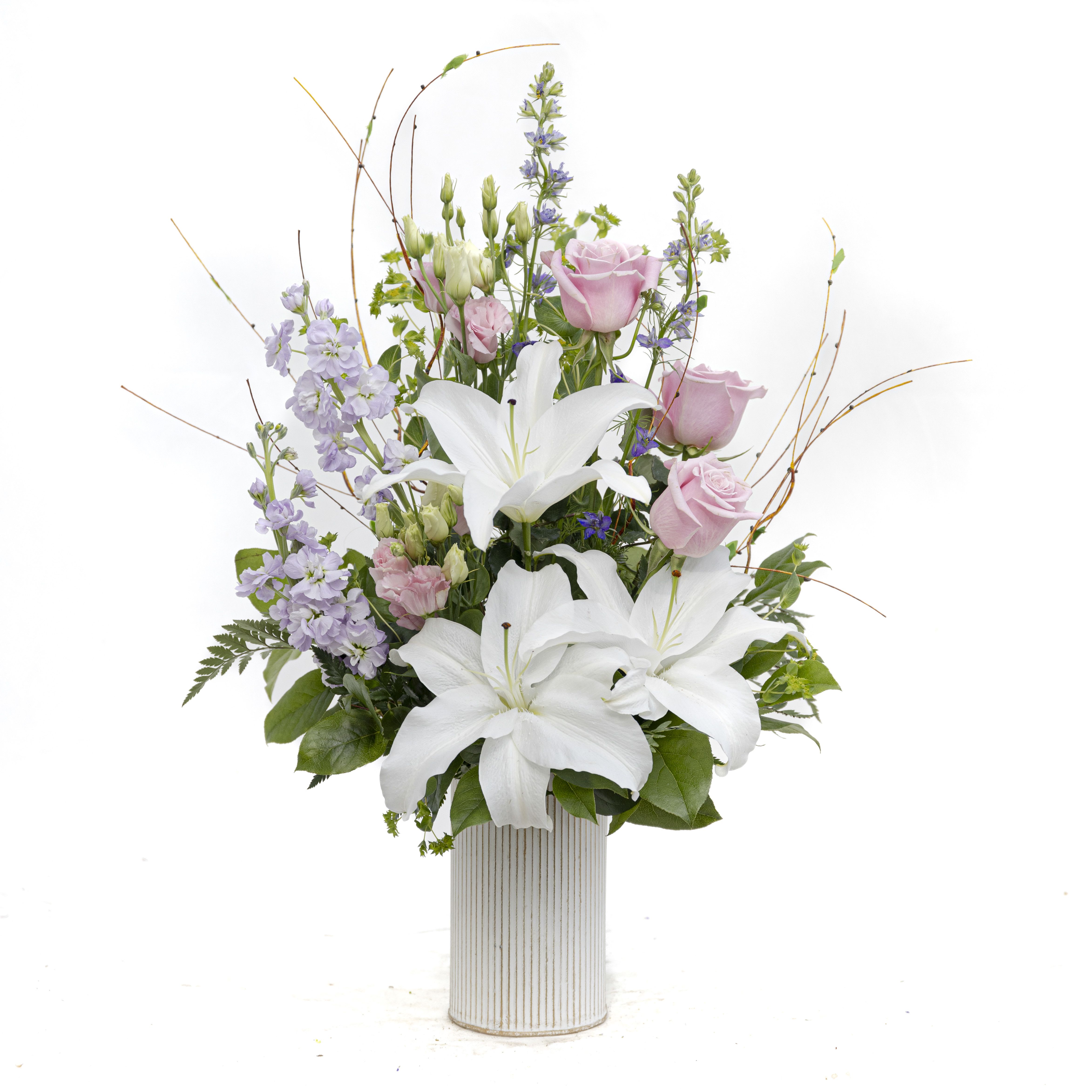 Sophisticated Love - A modern white wash metal container features a garden look of white Lilies, purple Larkspur, pink Lisianthus, lavender Stock and is accented with branch and Blupureum.