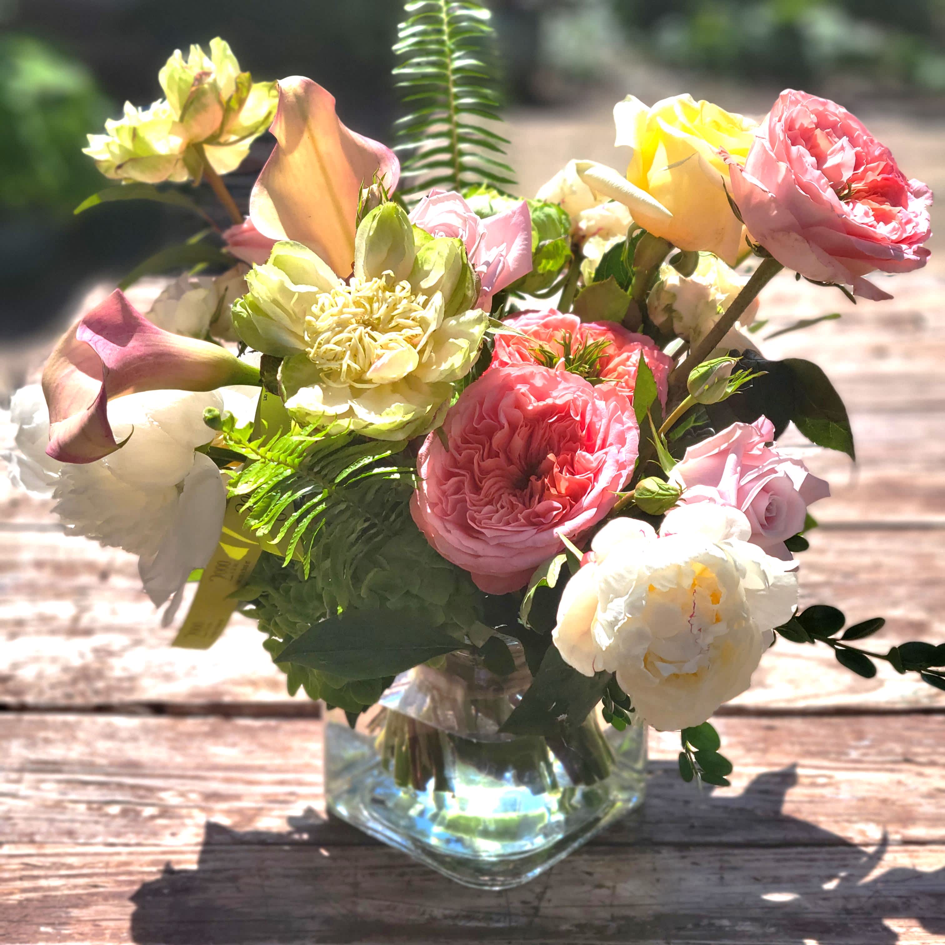 Charlie - Soft pastel floral mix in a variety of texture and depth accented with rich foliage and berries. Presented in a clear glass container with exposed stems.