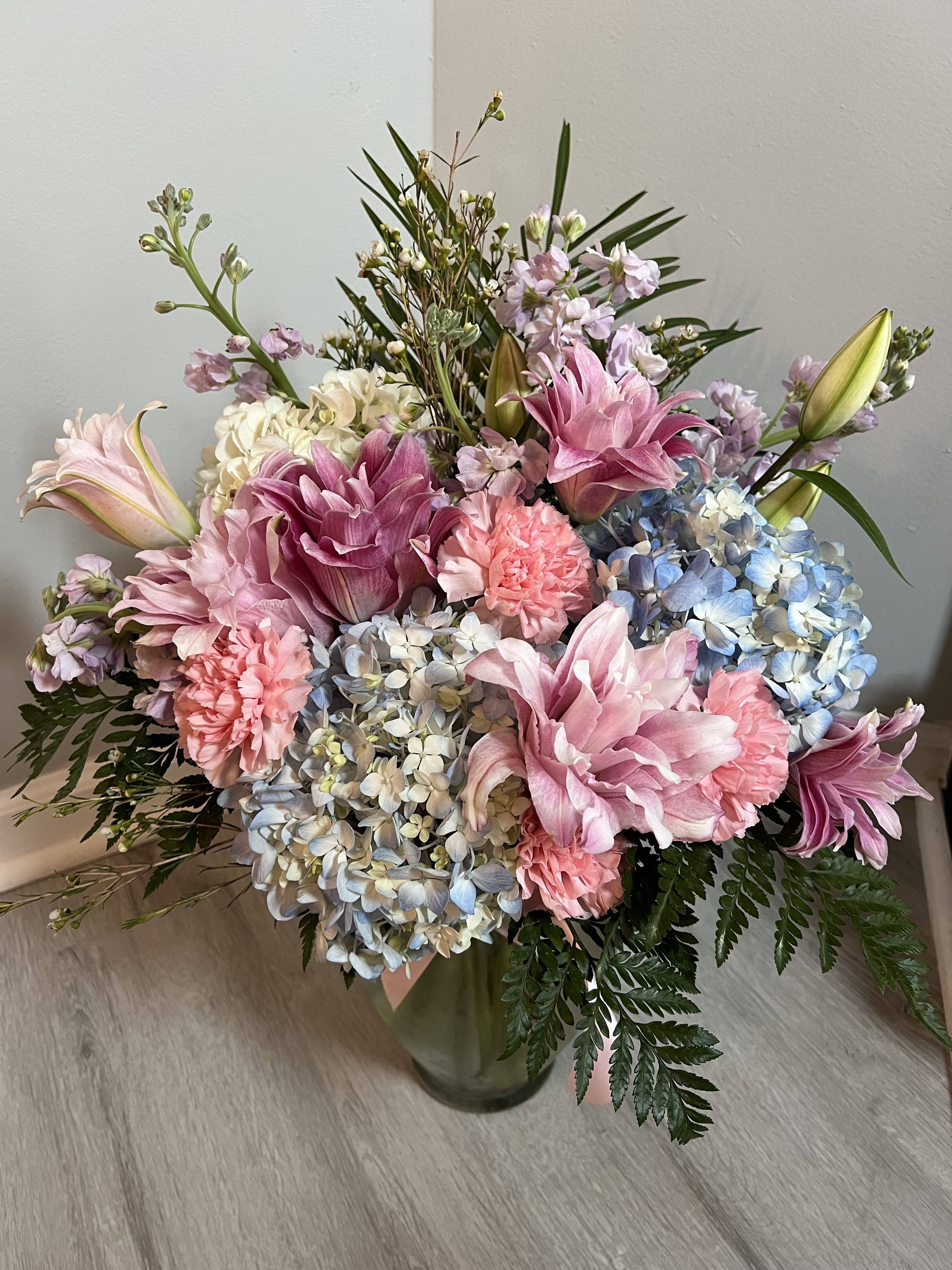 Above and beyond Above and beyond - Indulge in the beauty of this meticulously crafted floral arrangement, featuring a stunning blend of pink lilies, blue and white hydrangeas, white and pink seasonal blooms, and lush greenery. Perfect for adding a touch of elegance to any occasion, this arrangement is designed to captivate and delight.