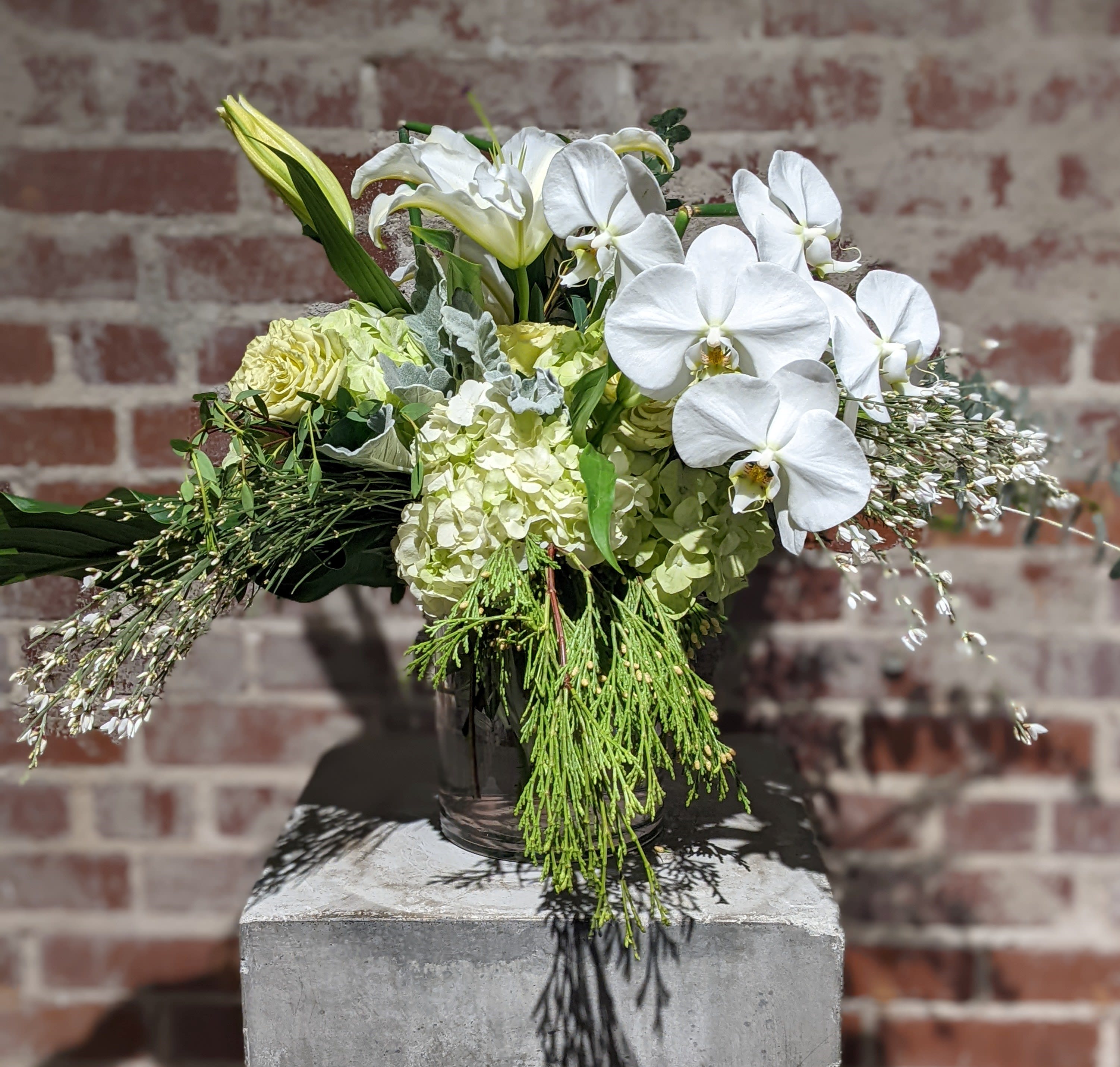 Limerick Limerick - Pastoral medley of greens and whites with assorted foliage accents. Presented in a clear glass container with exposed stems.