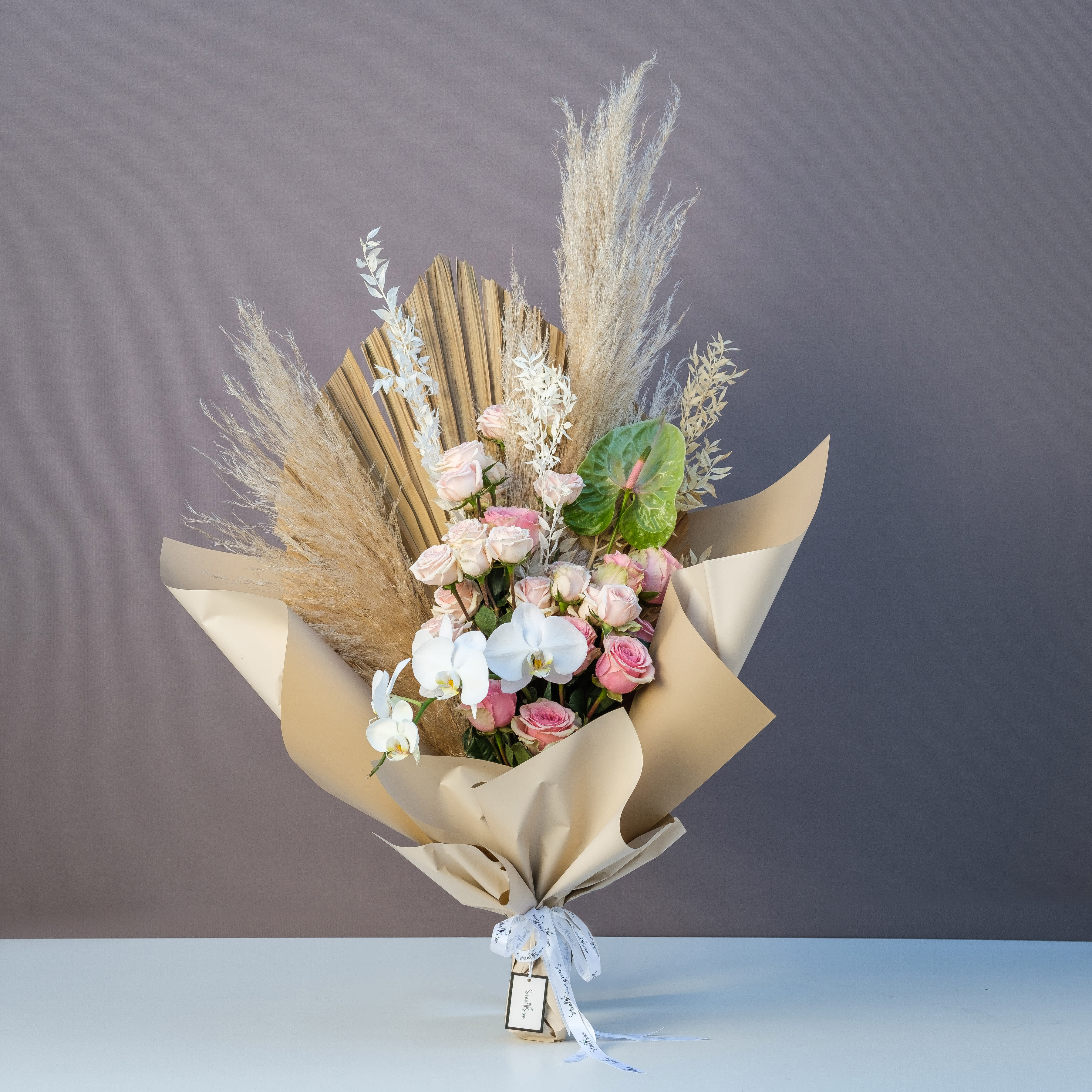 Boho Wrap Boho Wrap - A complete Bohemian wrapped bouquet that has a variety of unique textures and neutral tones featuring pale peach spray roses, peach and pink full size roses, an elegant white orchid stem, and more bohemian favorites including dried preserved greenery and natural palm leaf.