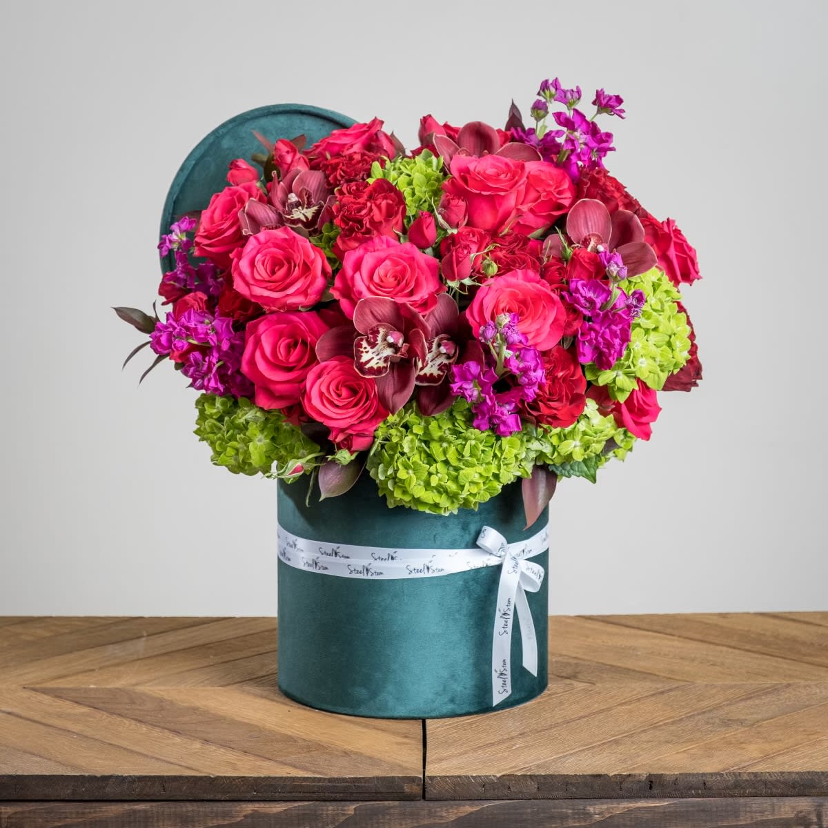 Jewel love Jewel love - A luxurious velvet green cylinder box is flourishing with emerald green hydrangeas, blooming pink rose and red roses, sweetly scented stock and wax flower, with touches of romantic red orchid blooms, and accented with a variety of fresh greenery. Our velvet green box has a finishing touch of our signature Steel Stem ribbon. Treat your special loved one this Valentine's Day to this gorgeous arrangement for a long lasting impression they are guaranteed to love forever! Measures approx. 24"H x 20"W