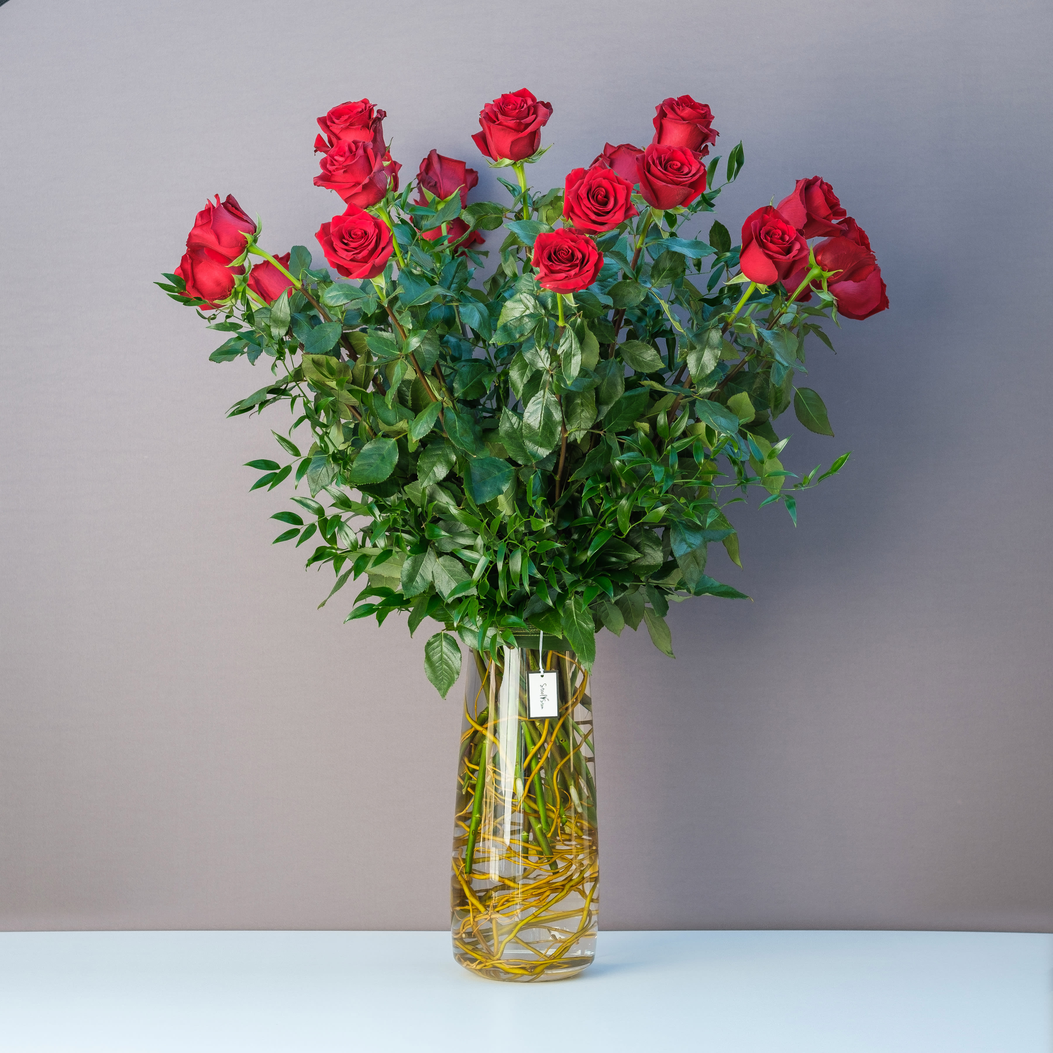 Two Dozen Long Stem Red Roses Two Dozen Long Stem Red Roses - A classic and elevated design of twenty-four long-stem red roses that is hand-created inside of a luxurious tapered glass cylinder lined with curly willow and with accents of complimenting lush greenery.