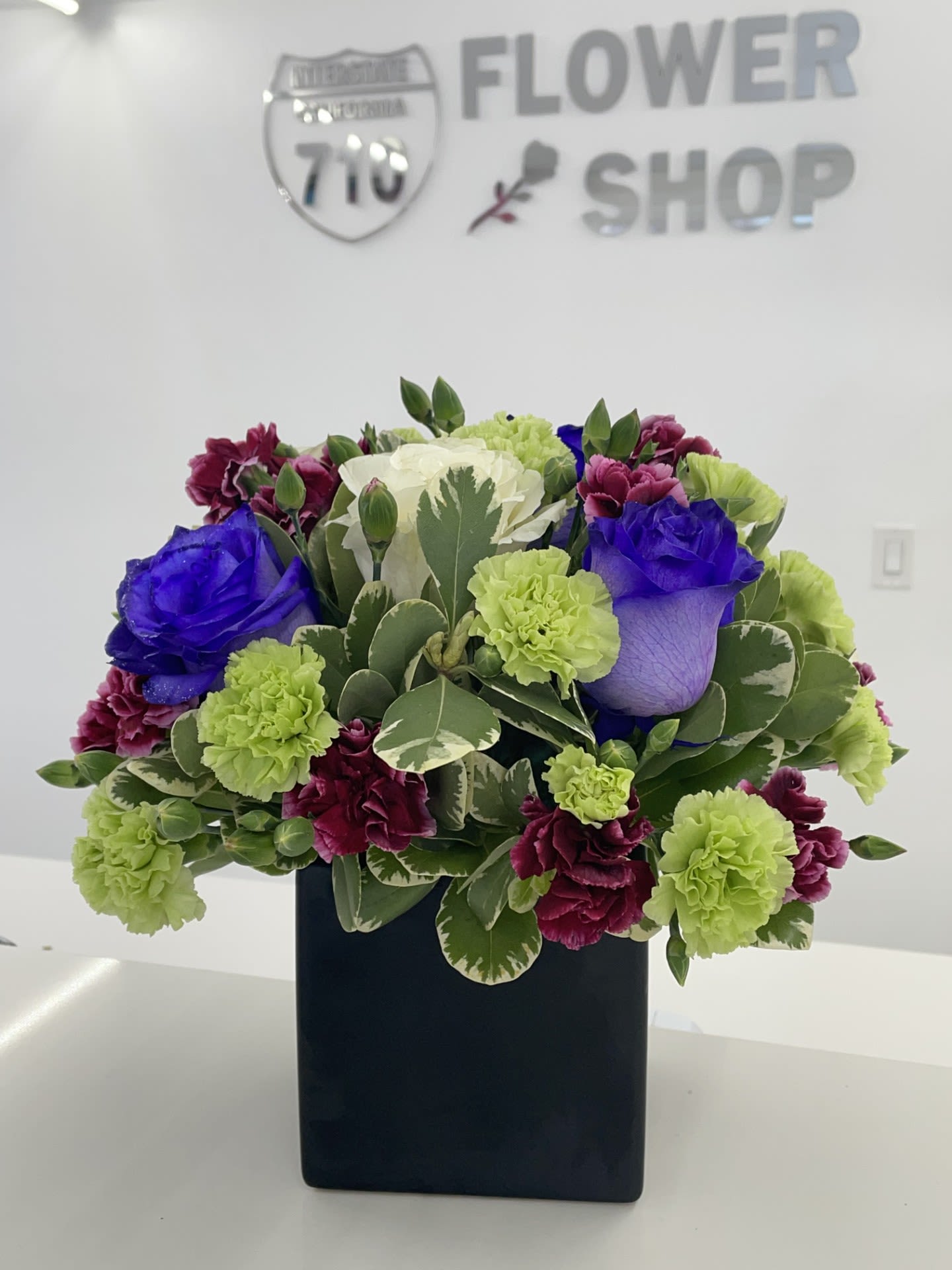Midnight Bloom  - The striking combination of deep purple roses, green carnations and mini carnations creates a dramatic and elegant palette- perfect for a statement gift or upscale event. (If you'd like to change any colors please leave note in instructions. If some flowers and/or the vase are not available there will be minor substitutions.)  