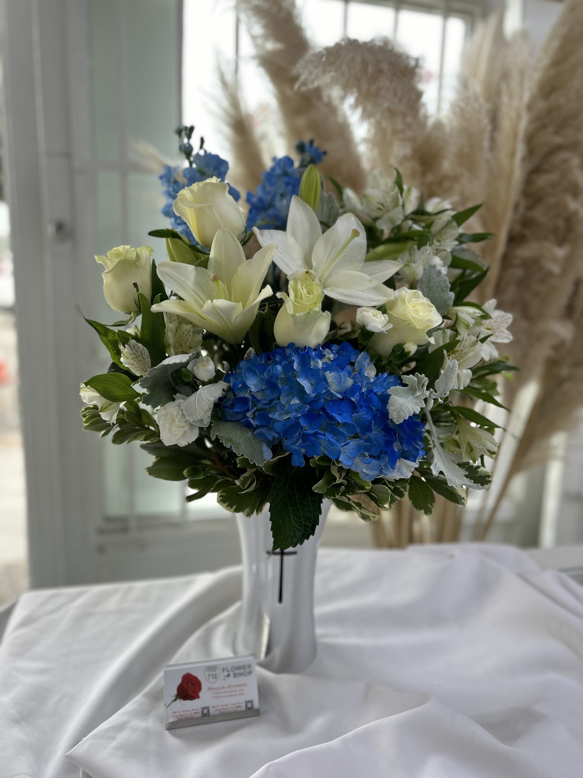 Ocean Breeze - The combination of blue hydrangeas, white lilies, and roses evokes a fresh and serene feeling, reminiscent of the sea and sky. The soft pampas grass adds a natural, airy touch. Substitutions: If some flowers and/or the vase are not available there will be minor substitutions. 