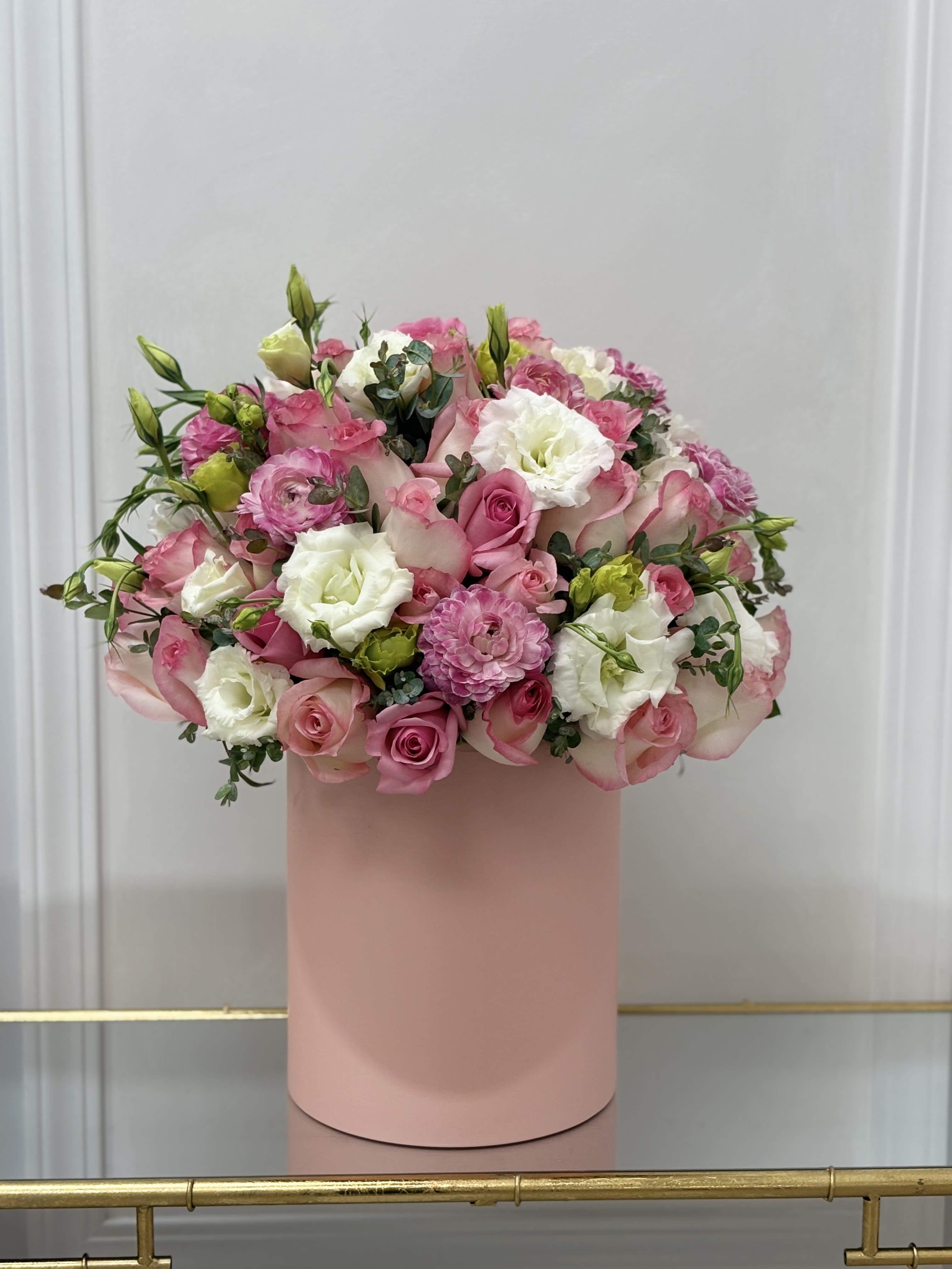 Miss Pinky Hat Box By VLM Flowers - This arrangement features pink ranunculus, soft white lisianthus, and pink roses.