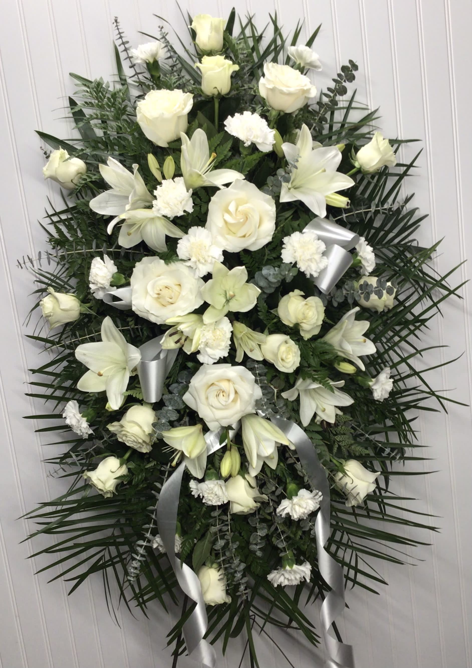 Sentiments of Serenity Spray - Beautifully simple this lovely spray of white roses lilies and carnations decorated with white satin ribbon is a tasteful way to express your sympathy. The elegant spray includes white roses white Asiatic lilies and white carnations accented with assorted greenery.Approximately 25&quot; W x 35 1/2&quot; H Orientation: One-Sided As Shown : T262-1A
