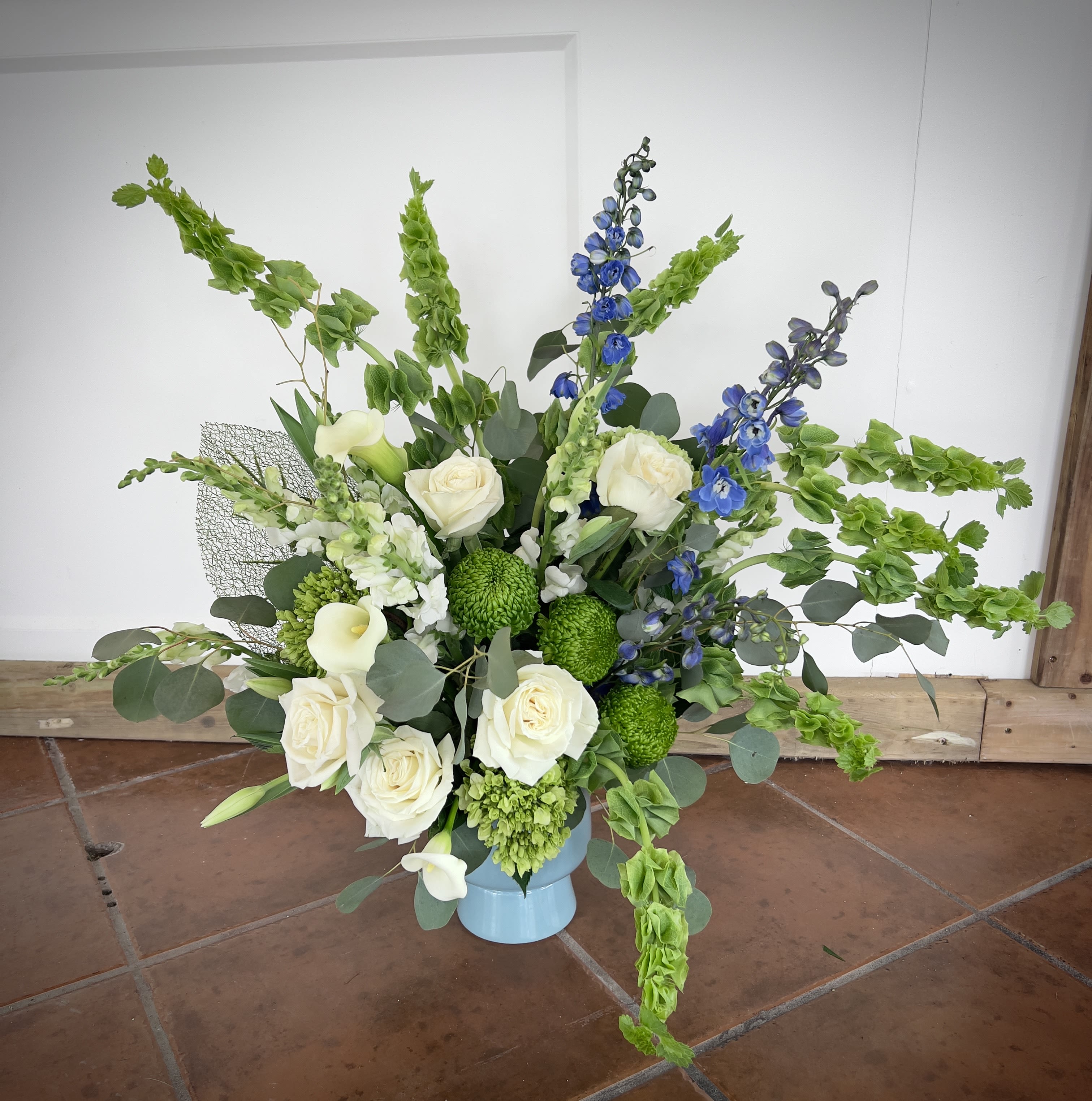 Flowing River by Bellas and Blooms Flowing River by Bellas and Blooms - This beautiful arrangement incorporates peaceful blooms adding the flow of a river to any room. From the flow of silver dollar eucalyptus to the hint of blue delphinium, you can feel the peace you get from watching a river flow. Finally Including other garden flowers such as Tulips, White roses, White Callas, Bells of Ireland, and Alstroemerias you allow nature's peace to flow into your loved ones * The Vessel the arrangement is created in is subject to substitutions based on vessel inventory.