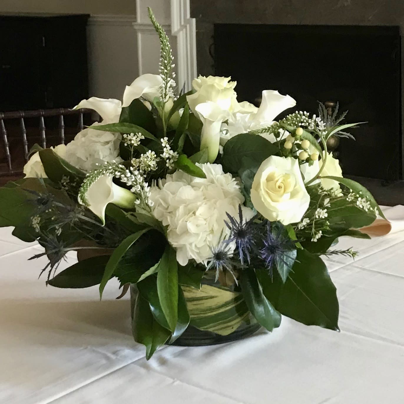 The White Collection The White Collection - This serene arrangement is made up of a variety of white flowers including white hydrangea, white roses, calla lilies, lysimachia, white hypericum berries, white wax flower and blue thistle. The clear glass container will be lined with a ginger leaf. Your arrangement will be designed in the style shown but flowers and containers may be slightly different from that pictured. Floral designers make every effort to use the best floral selection of the day.