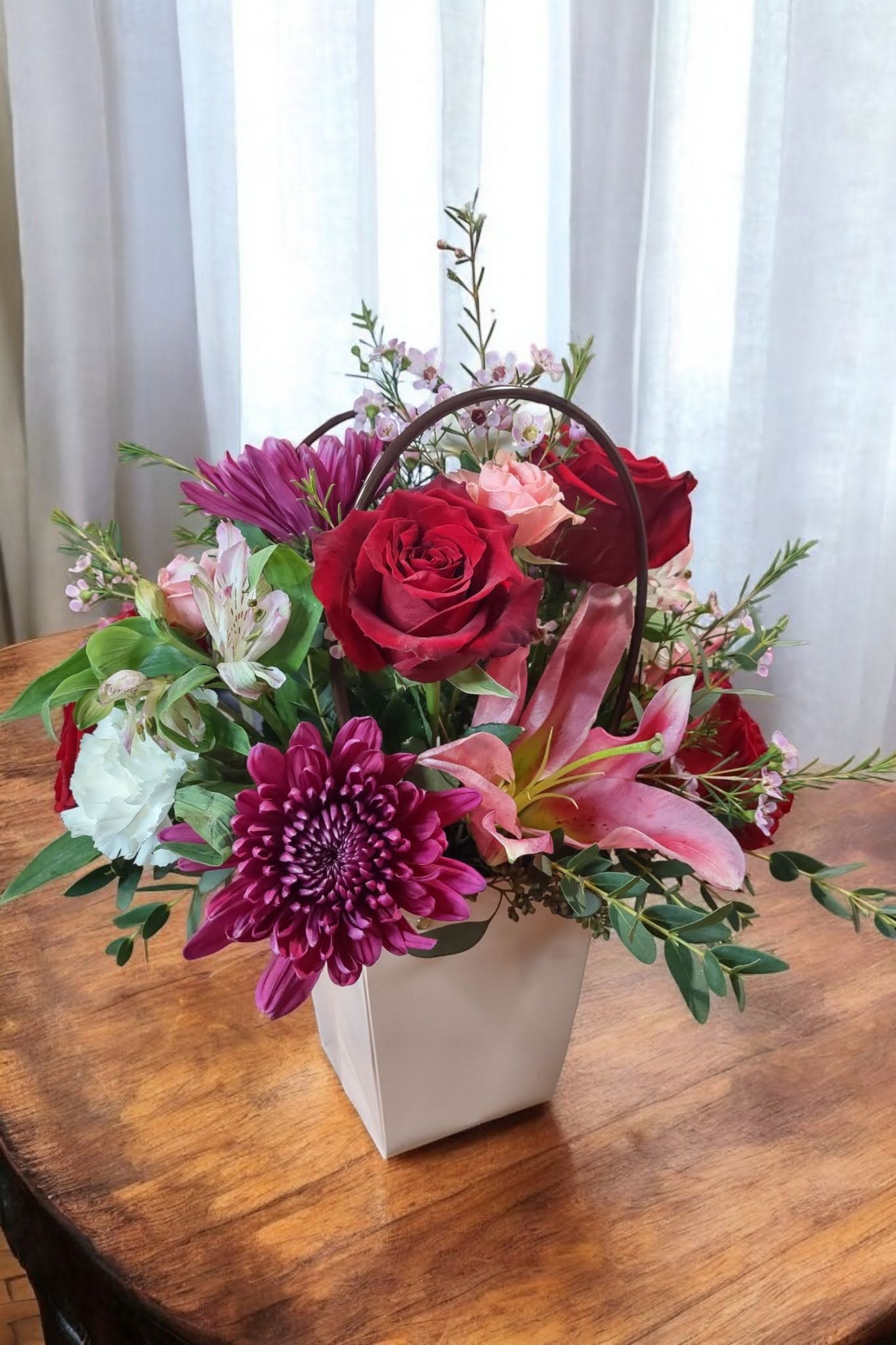 Carrying Your Love With Me Carrying Your Love With Me - "Carrying You Love With Me" is a vibrant and passionate flower arrangement that embodies the powerful sentiment of love and devotion. Set in a decorative tote, the bouquet features stunning pink lilies, their elegant, trumpet-shaped blooms symbolizing beauty and the delicate nature of love. Deep red roses, rich with meaning, bring a sense of passion and romantic intensity to the arrangement. Interspersed with soft pink, bold red, and pristine white flowers, this mix creates a harmonious balance of affection, longing, and purity.