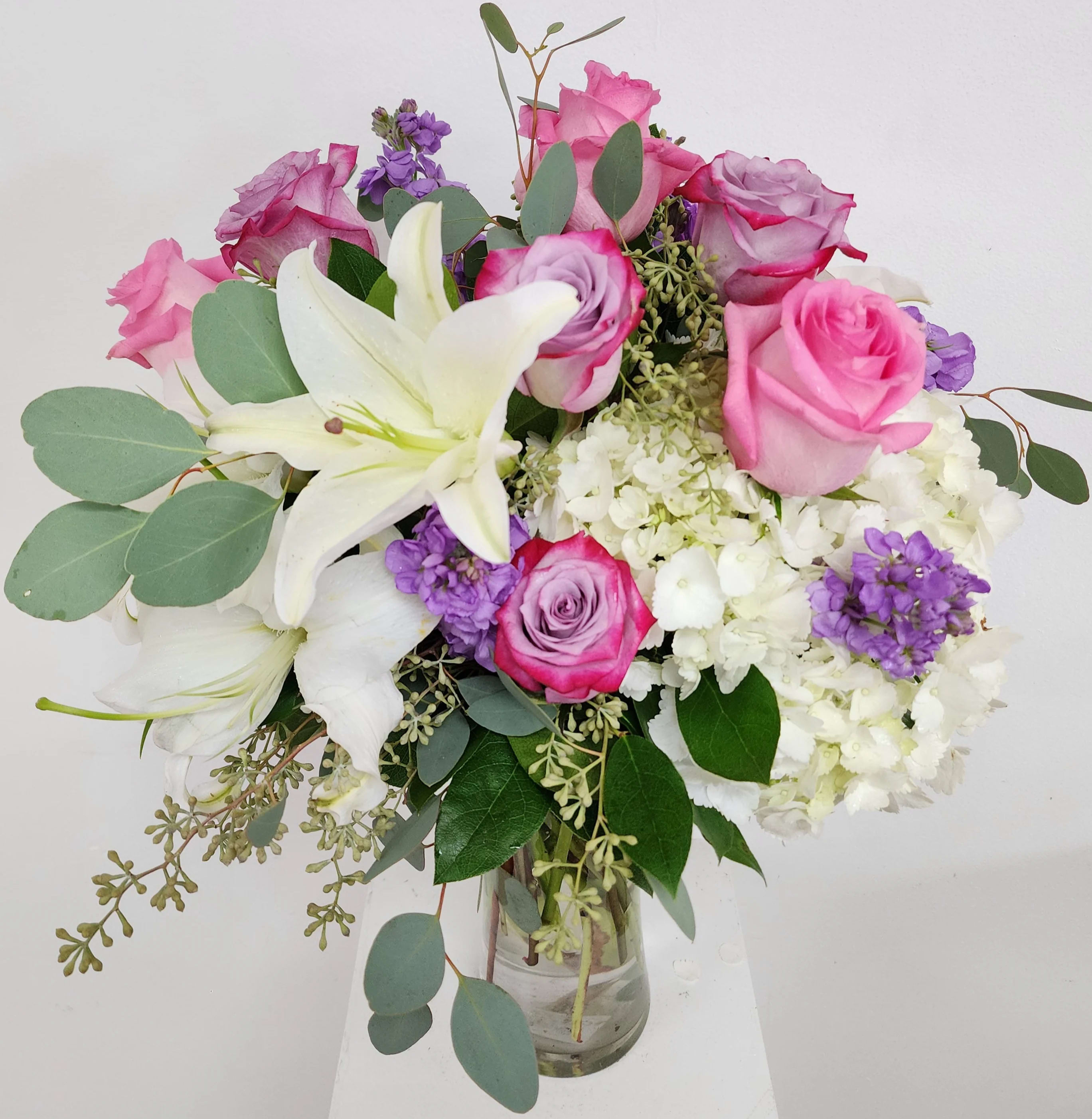 Hermosa Bouquet - Hermosa or pink roses, lavender roses, lavender stock, hydrangea, wax and silver dollar in a clear vase. 