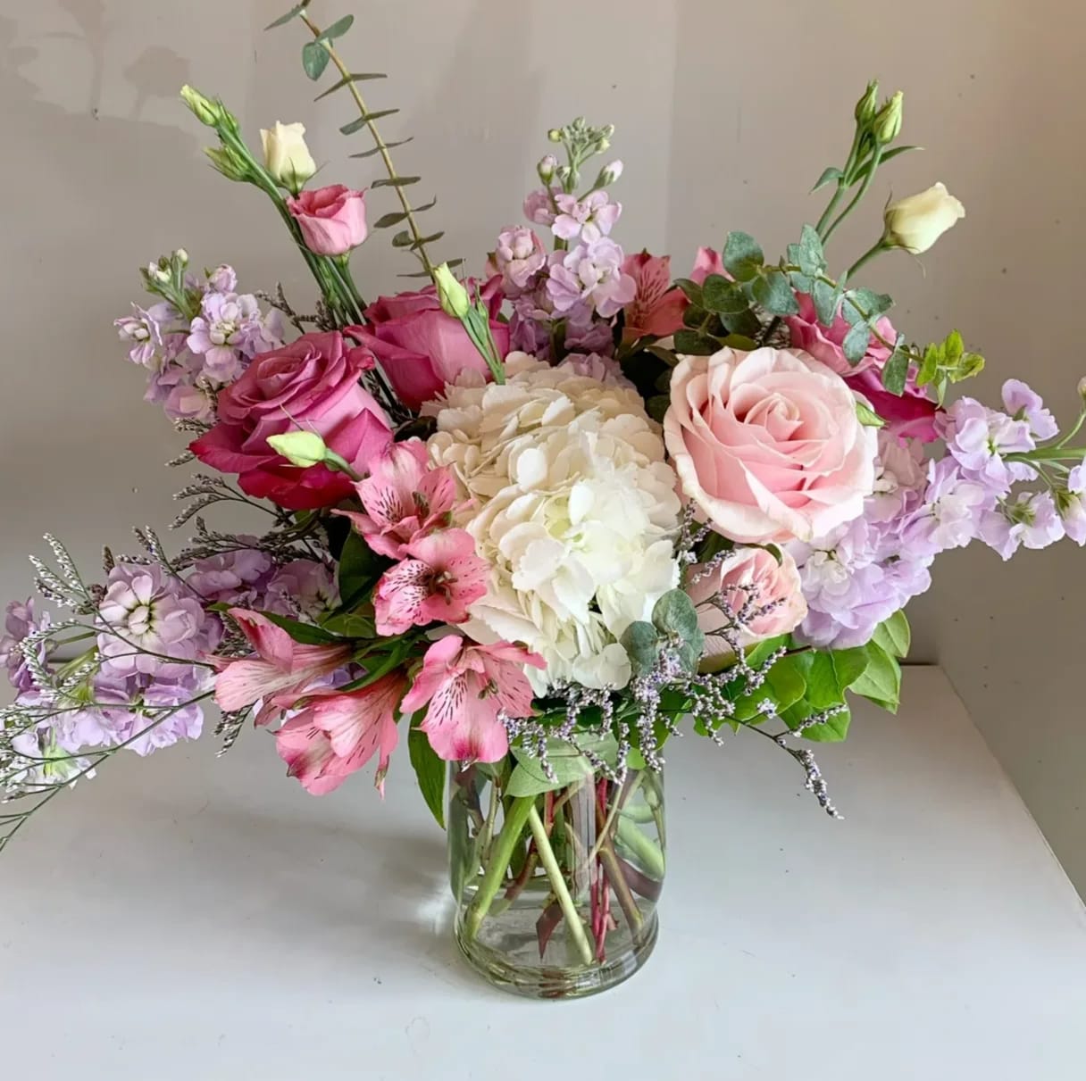 Pipa - Sweet Pipa features gentle blush roses and pristine white hydrangeas, with a touch of lavender stock and ocean song roses. This elegant arrangement is beautiful gathered in a clear hurricane case. 