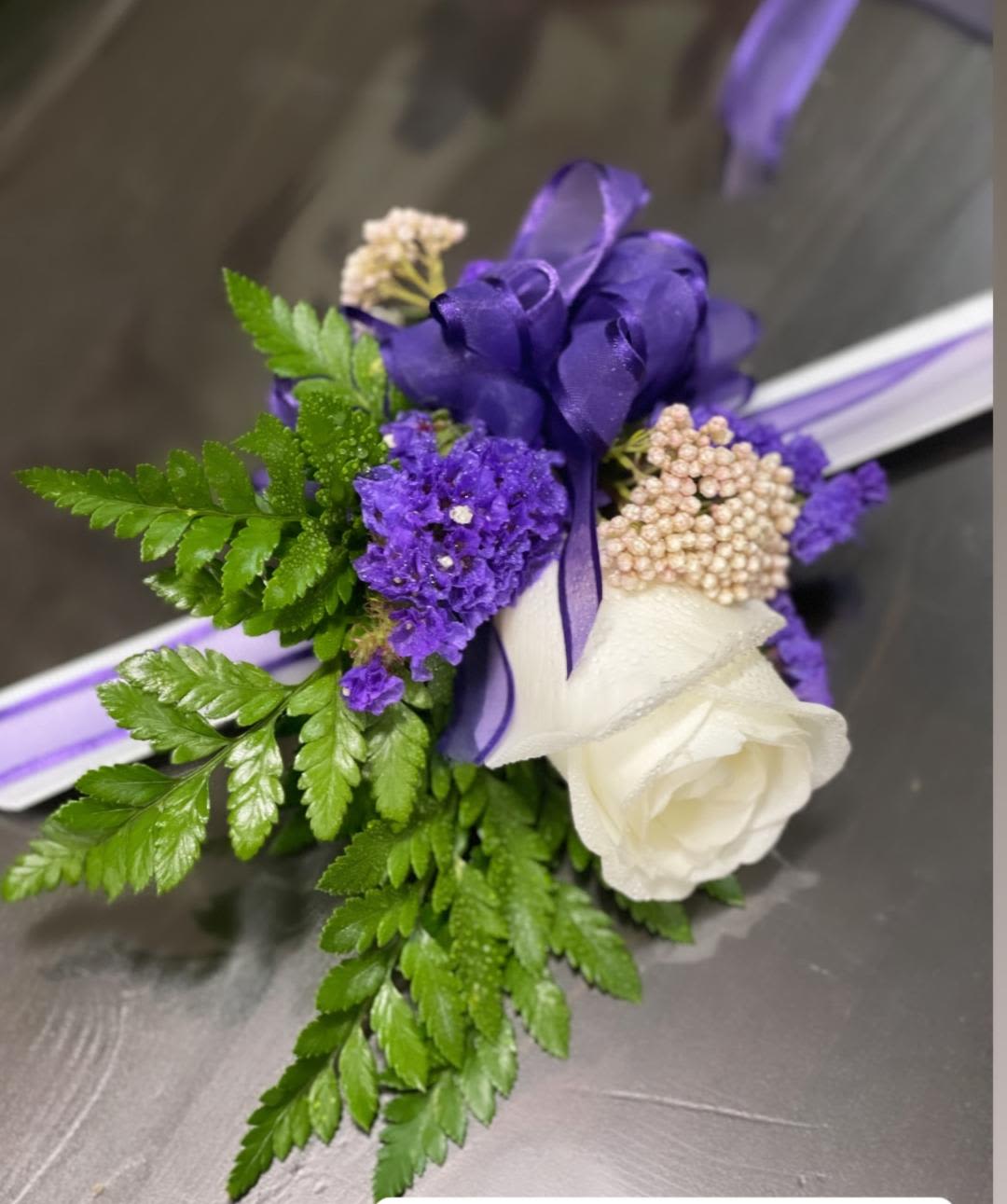 Violet Galore Corsage - Made from fresh flowers, a corsage looks like a petite flower arrangement (typically consisting of just one or several smaller blooms) and usually sits on the wrist like a bracelet, though it can also be pinned on a lapel. Corsages serve as a way to honor people who are very important to the couple getting married. Please contact our shop at (747) 249-4678 for any customization. 