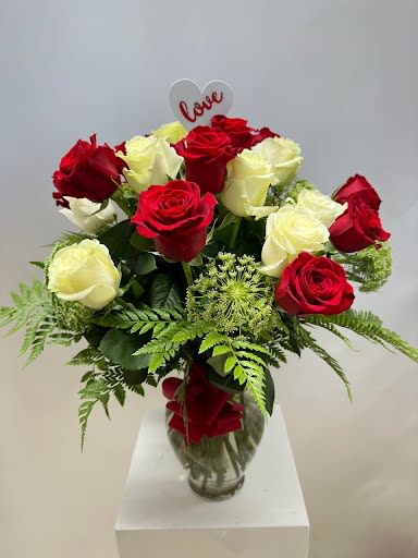 A MOTHER'S Touch  - This floral arrangement is a stunning modern romance captured in a vase. The rich red and creamy white roses speak of timeless love and passion, while the elegant greenery adds a fresh, contemporary touch. The heart-shaped “love” sign at the top is a perfect finishing detail—playful, bold, and heartfelt. It’s a bouquet that says “You are my today and all of my tomorrows” with grace and sophistication.