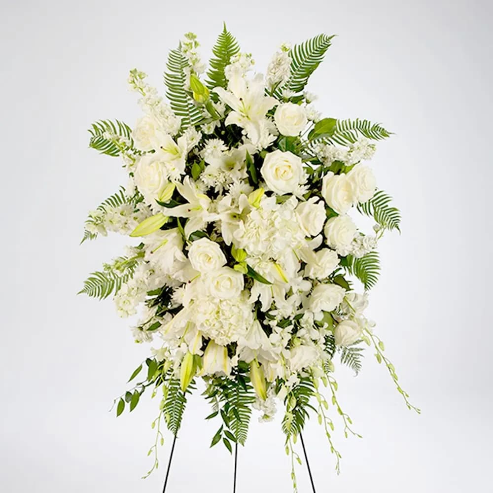 True Sympathy  - Create a serene and elegant atmosphere at your loved one's service with our exquisite all-white standing spray. This stunning arrangement combines the timeless beauty of white roses, stock, hydrangea, dendrobium orchids, and lilies, coming together to form a breathtaking tribute of purity, love, and serenity.