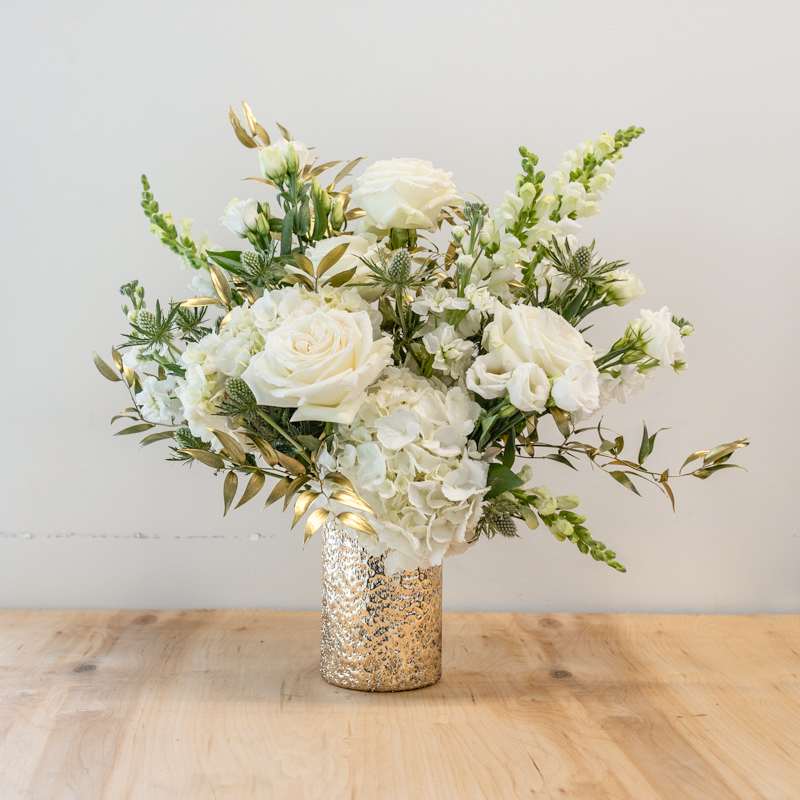 Athena Athena - A powerful combination of crisp, clean white, cream, and gold.  Hydrangea, Garden Roses, Lisianthus, fragrant Stock, Snap Dragons, and Gold Dipped Greenery.  Comes in a golden container - Approximately 14 H x 12 W - Photo shown is of the DELUXE price point.