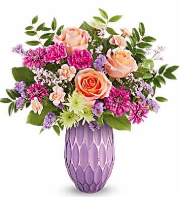 Pretty Glow - Make her Mother's Day or any day. Shine with Teleflora's Pretty Glow Bouquet, featuring a stunning mix of roses, carnations, and chrysanthemums, beautifully presented in a sculpted glass vase with a purple mercury-inspired finish. A perfect blend of elegance and charm to brighten her special day.  Peach roses, fuchsia carnations, peach miniature carnations, green cushion spray chrysanthemums, purple cushion spray chrysanthemums, purple sinuata statice, and pink limonium are artfully arranged with huckleberry and salal in Teleflora's Pretty Glow vase, creating a stunning Mother's Day or any day bouquet.