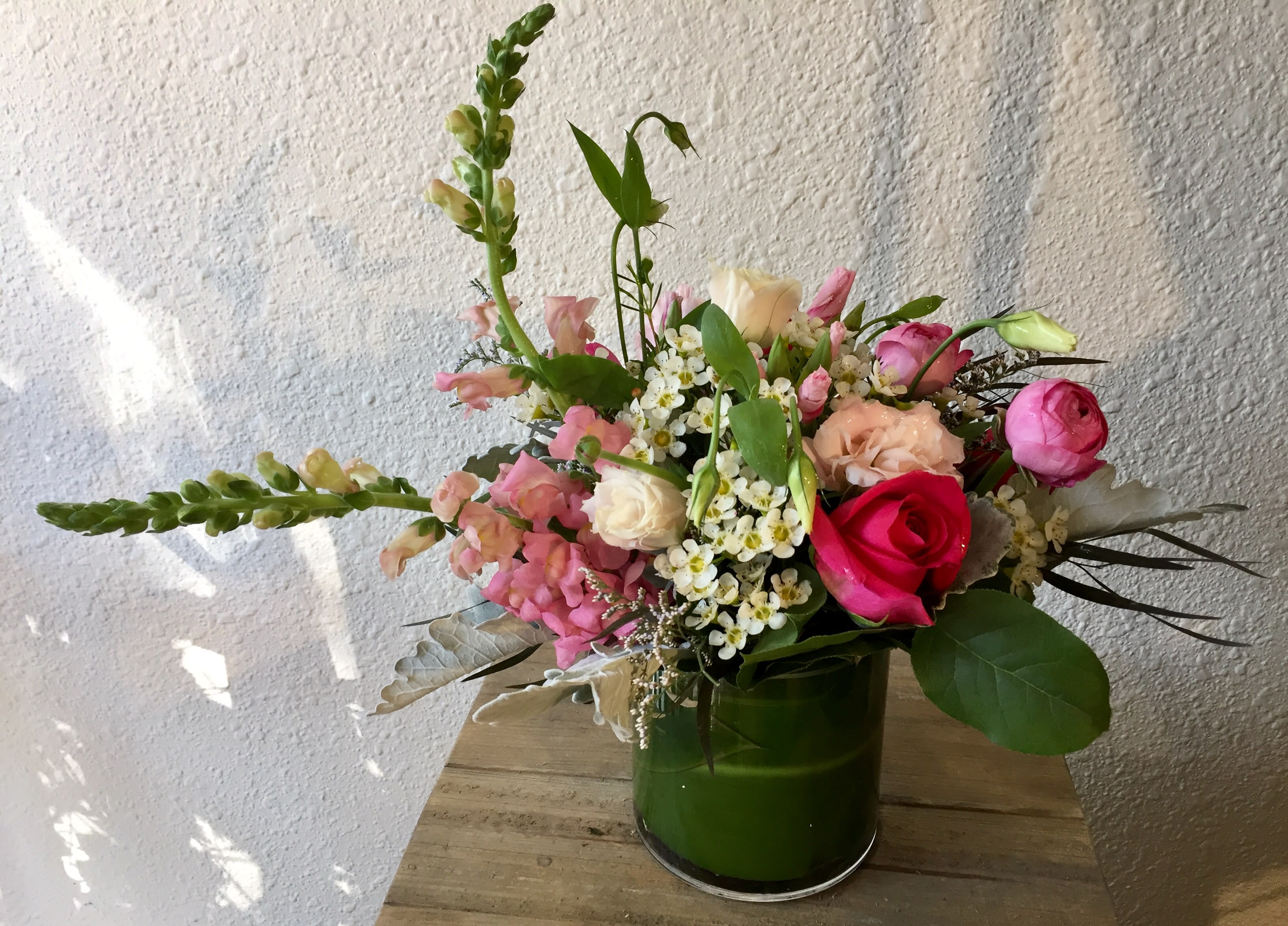 Pure Pink Pure Pink - Snaps, ranunculus, roses and lisianthus in a leaf wrapped cylinder, very simply placed, providing a beautiful centerpiece for all occasions.