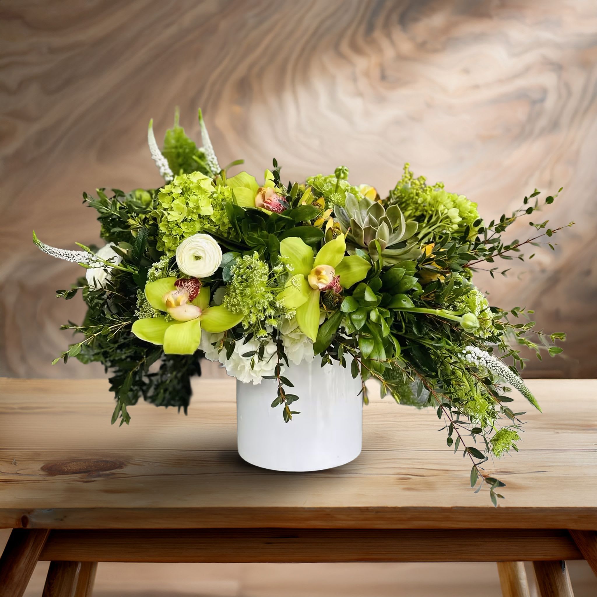 Emerald Whisper <3 Emerald Whisper <3 - Bold, organic, and undeniably elegant, this lush green and white floral arrangement delivers an upscale botanical experience perfect for the modern aesthetic. Presented in a sleek matte white ceramic cylinder vase, this artfully asymmetrical design bursts with premium blooms and layered greenery that create movement and texture from every angle. Featuring vibrant green cymbidium orchids, creamy white ranunculus, white veronica, and touches of soft blush lisianthus, the palette is elevated with lush green hydrangeas and unique seasonal filler flowers. Cascading foliage such as seeded eucalyptus, ruscus, and wispy fern add dramatic flow, giving the entire piece a dynamic garden-style feel that feels both intentional and wild. This designer arrangement is ideal for contemporary home interiors, high-end office installations, modern wedding tablescapes, or green-forward events. Its organic elegance and natural flow make it a favorite for corporate clients, stylists, and discerning floral lovers seeking a statement piece that breaks from tradition. Whether you're sending a gift to impress, decorating a modern lobby, or elevating a dining table with fresh florals, this composition brings nature-inspired refinement to any space. Touch of Orchids LA proudly delivers this green and white orchid-focused arrangement across Los Angeles, including Beverly Hills, West Hollywood, Pacific Palisades, Santa Monica, and the greater LA region. Available for same-day delivery.