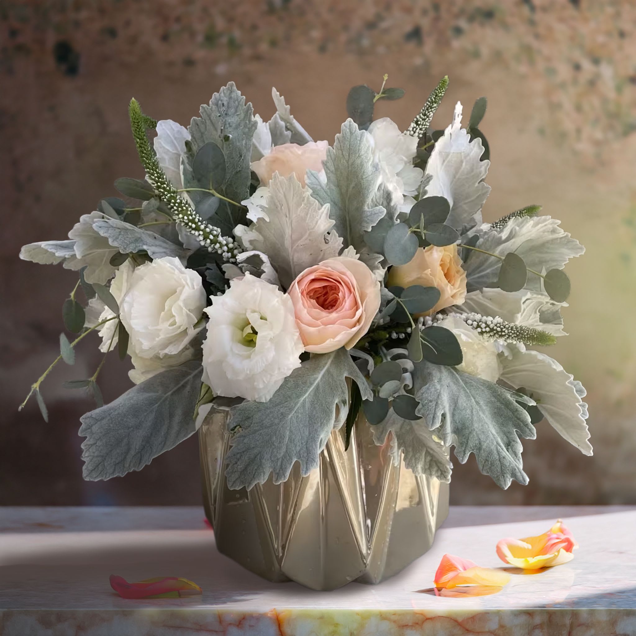 Glistening Garden <3 Glistening Garden <3 - Modern minimalism meets soft romance in this elegant neutral-toned floral arrangement. Set in a metallic faceted ceramic vessel with a subtle sheen, the composition pairs creamy white lisianthus, soft peach roses, and pale blush spray roses with cascading sprigs of eucalyptus and velvety silver dusty miller. Textural white veronica adds gentle verticality, while the overall color palette remains cool, muted, and sophisticated. The sculptural shape and tone-on-tone style make this a standout piece for modern design lovers and luxury interiors. Perfect for contemporary homes, corporate gifting, art galleries, or minimalist weddings, this arrangement evokes tranquility, class, and subtle luxury. It’s ideal for styling on a coffee table, nightstand, or reception desk where beauty is appreciated in clean, intentional forms. Whether sent as a sympathy gesture, stylish thank-you, or just-because gift, this floral piece offers quiet elegance with timeless appeal. Touch of Orchids LA offers same-day flower delivery throughout Los Angeles, including Beverly Hills, West Hollywood, Malibu, Santa Monica, and Downtown LA. This arrangement is especially popular among interior designers, creative studios, and modern hospitality suites.