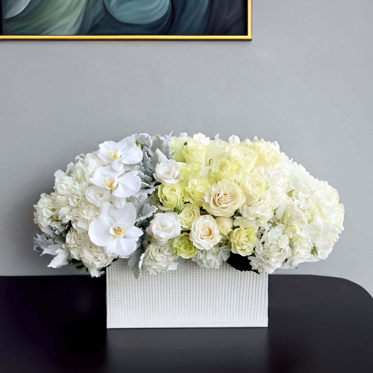 Grand Entrance Grand Entrance - Pure, elegant, and immaculately composed, this all-white floral arrangement is the ultimate expression of luxury minimalism. Designed in a modern white ribbed ceramic vessel, this lush composition features an exquisite blend of premium white blooms including hydrangeas, ivory and cream roses, white lisianthus, phalaenopsis orchids, and soft dusty miller foliage. The shape is wide and low, with a full dome of tightly clustered florals that deliver both softness and striking presence — perfect for refined interiors, milestone moments, or heartfelt sympathy gifts. This arrangement is ideal for weddings, condolence offerings, corporate gifting, or sophisticated home décor. With its clean palette and flawless design, it complements both modern and traditional spaces with quiet opulence. Whether styled in a gallery-like setting, used for luxury real estate staging, or sent to express a message of grace and remembrance, this piece speaks volumes in its simplicity. Touch of Orchids LA offers same-day flower delivery of this white floral arrangement throughout Los Angeles, including Beverly Hills, Bel-Air, West Hollywood, Pacific Palisades, and Brentwood. It’s a staple of our Signature White Collection and a client favorite for upscale occasions where elegance is essential.
