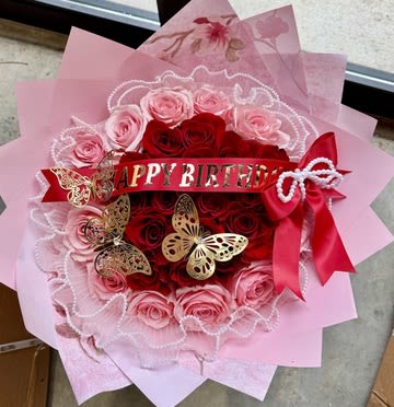 Butterfly Kisses Birthday Bouquet - Make birthdays unforgettable with the Butterfly Kisses Birthday Bouquet — a stunning medley of romance and celebration. This arrangement features velvety red and blush pink roses elegantly layered in a circular design, accented with pearl detailing, golden butterfly ornaments, and a bold “Happy Birthday” banner. Finished with rich pink wrapping and a satin bow, this bouquet is a show-stopping gift for someone truly special.