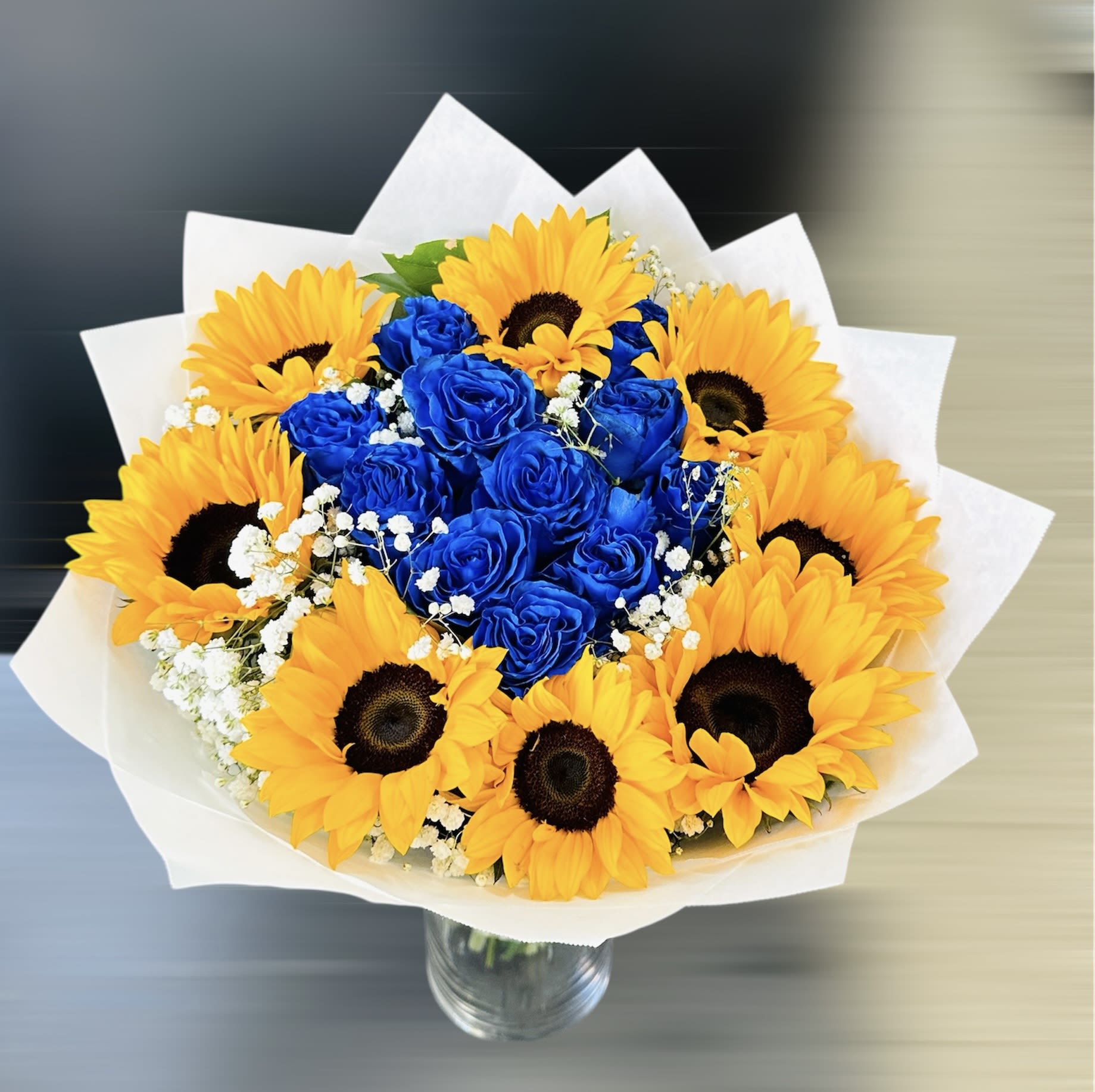 Golden Skies - A bold and vibrant bouquet featuring golden sunflowers, royal blue roses, and delicate baby’s breath. 