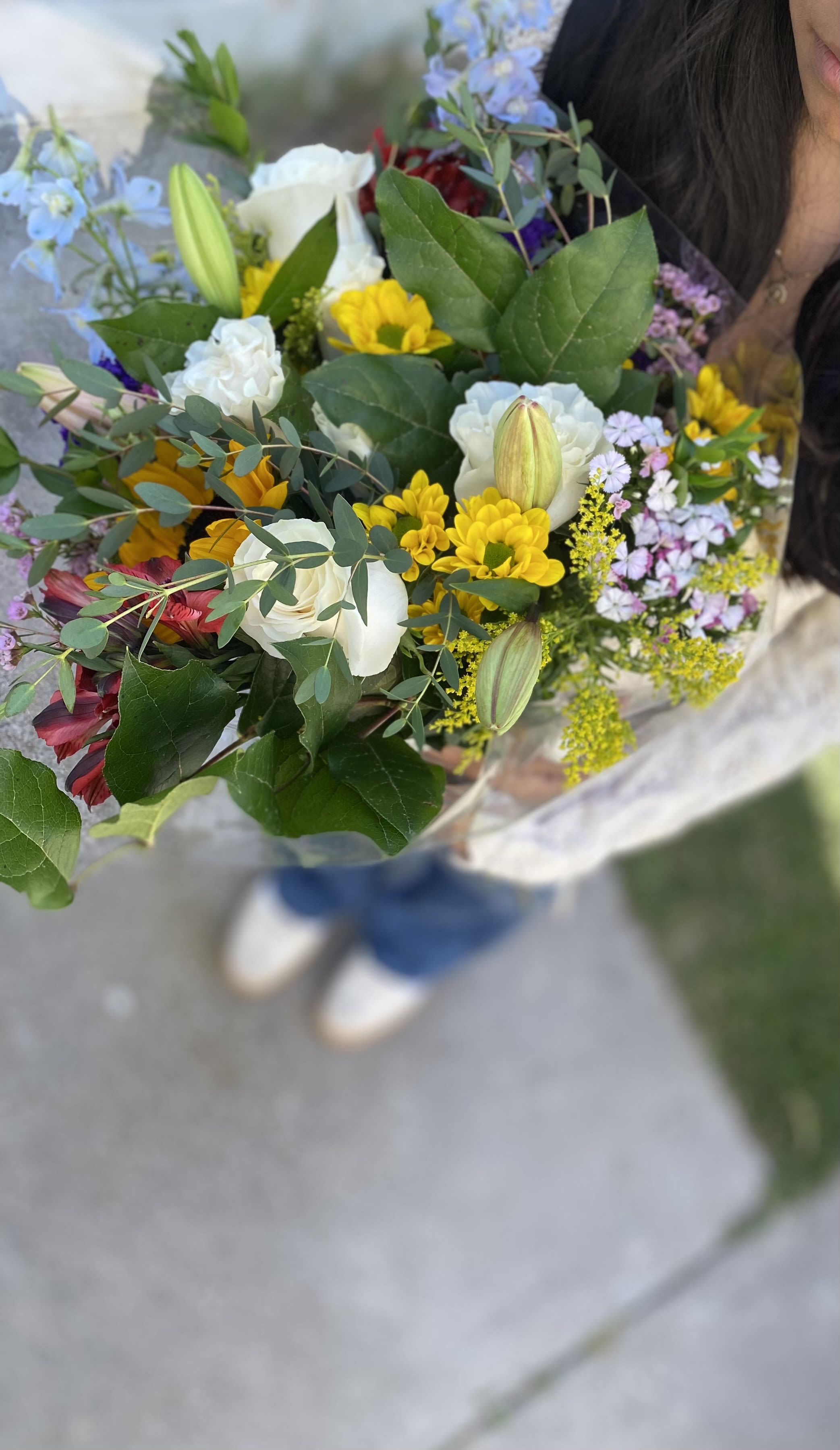 Liella  - Traditional bouquet of white roses, daises, lilies, sunflowers, Alstroemerias and other blooms. Hand wrapped in plastic with ribbon . Please note: This bouquet can be substitute for Kraft paper.