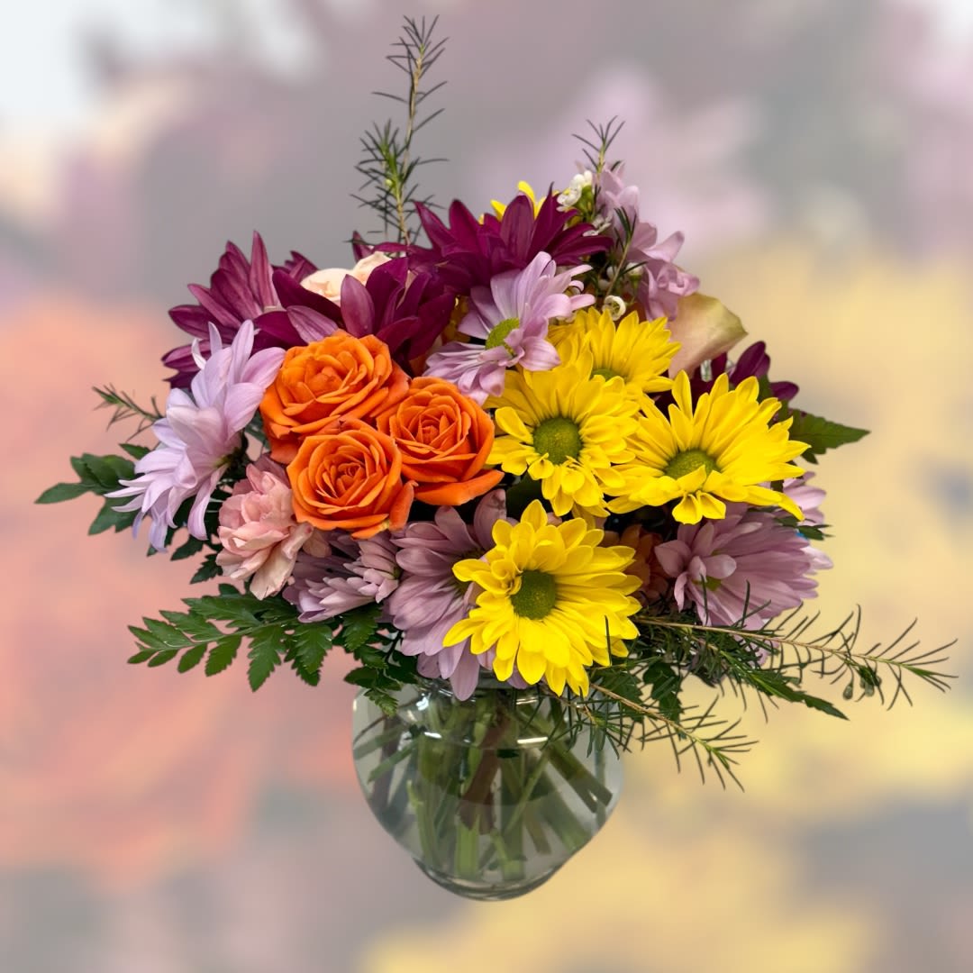 Marguerite Marguerite - Simple, sweet, and perfect for small spaces. A variety of colors and flowers in a clear glass 4" urn. (Arrangement is Approximately 9" tall)