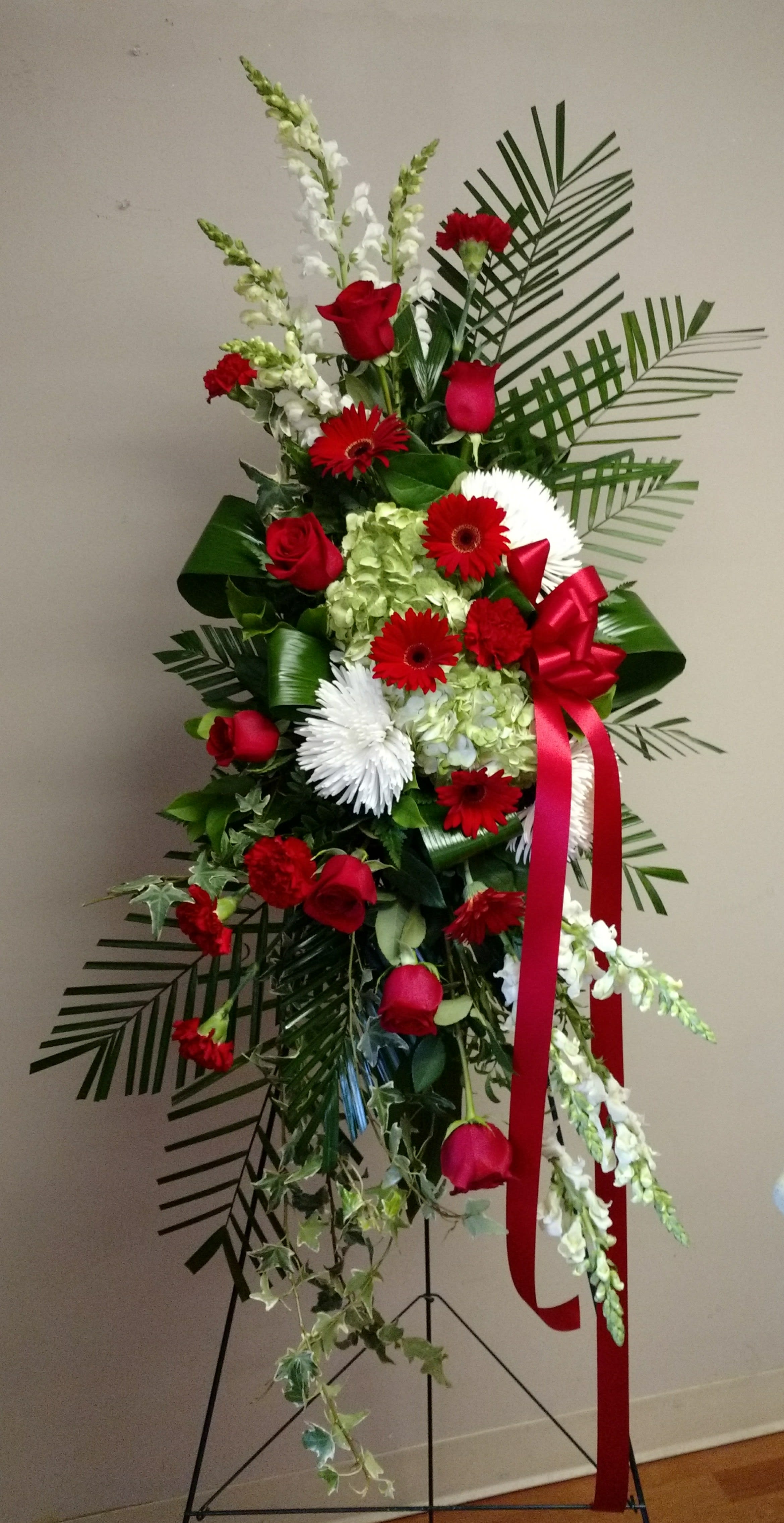 Fondly Remembered by Candlelight & Roses Fondly Remembered by Candlelight & Roses - A stylized easel spray of red, whites and a variety of foliage. Featuring snapdragon, roses, gerbera, hydrangeas, carnations and spider mums.