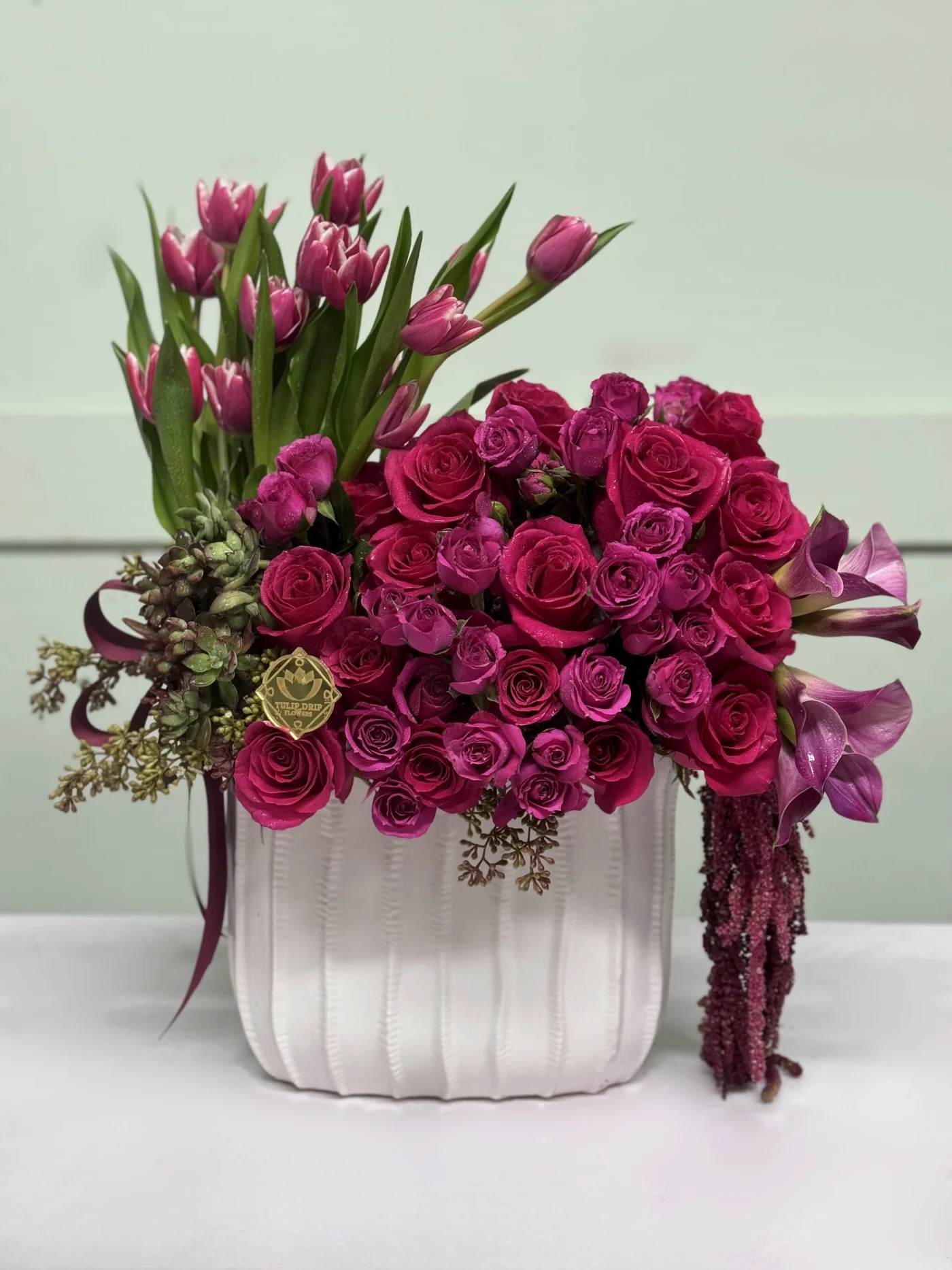 Hot Pink Rose  #1  - Vibrant hot pink roses, spray roses, Calla Lilies, Tulips, and Succulents arranged in a chic white ceramic vase, creating a lively and stylish centerpiece.